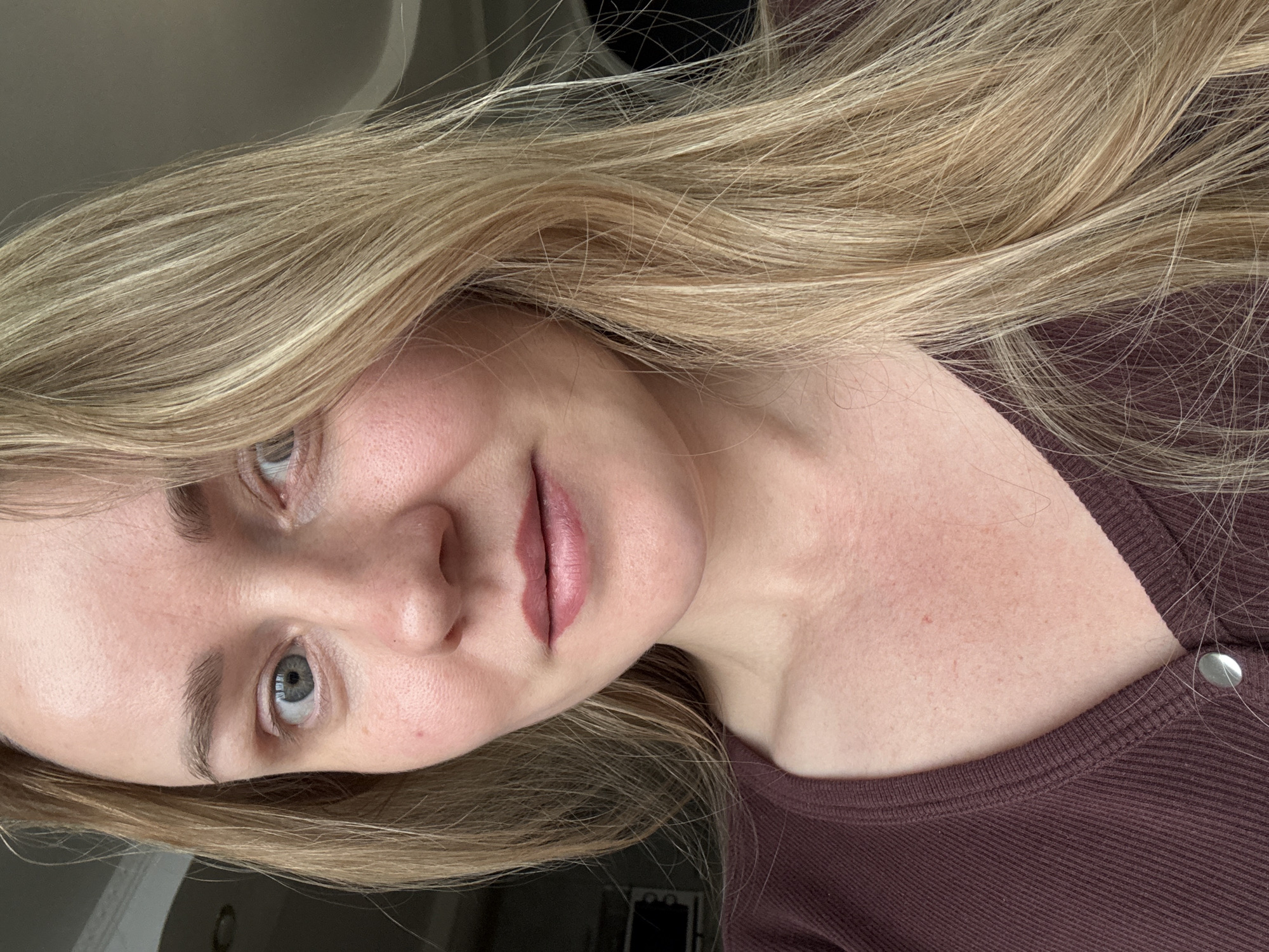 A photograph depicts a woman with fair skin and light blond hair, wearing a maroon-colored, ribbed shirt. Her head is tilted to the right. The setting is undefined. There is no information available to determine if the image was taken in the city of Chaikovsky, Russia.