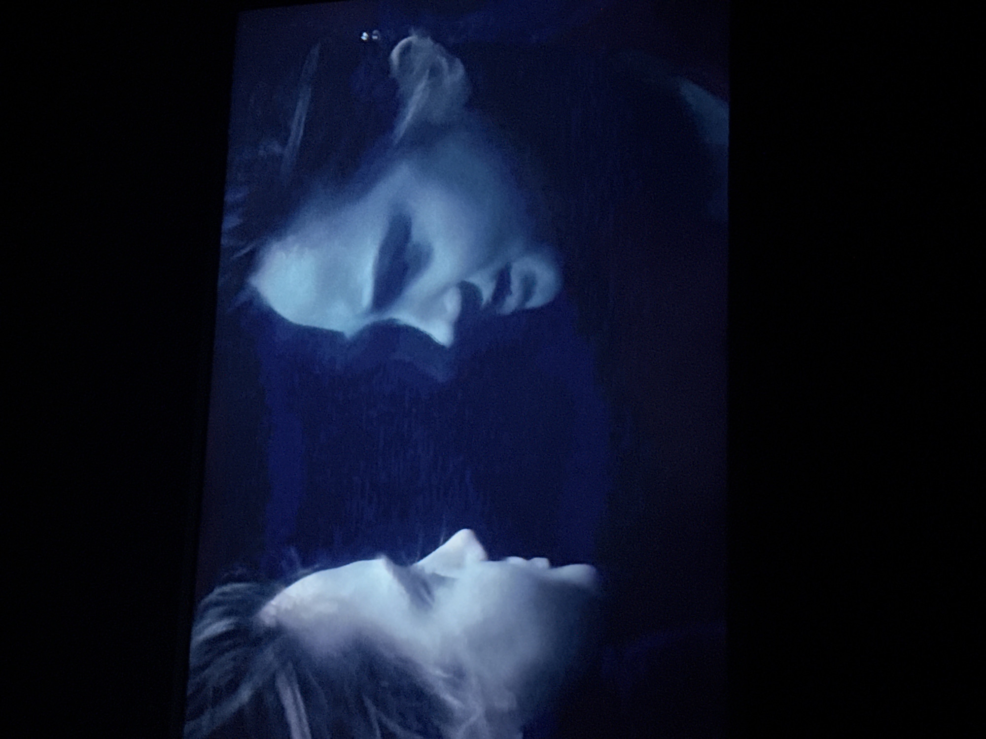 The image appears to be a still from the movie "Titanic." It depicts Jack and Rose, played by Leonardo DiCaprio and Kate Winslet, in a scene where Rose is floating on a door in the cold water after the ship has sunk, while Jack is in the water beside her. The image is dark and blue-toned, reflecting the cold water and the night. The location information is not relevant to the image.