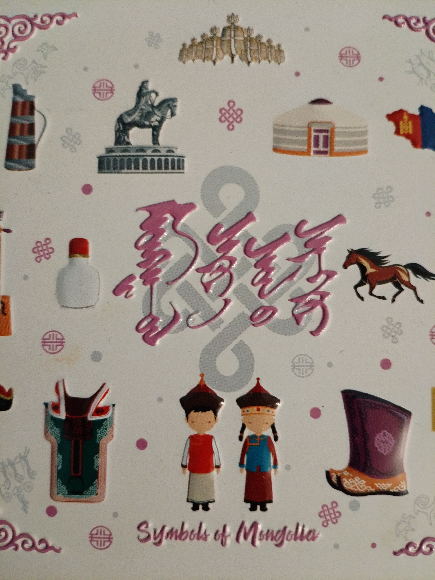 The image is a decorative, embossed surface, likely a souvenir or packaging, featuring various symbols and illustrations related to Mongolian culture. In the top section, there's an image of a monument with a figure on horseback, a yurt, and a stylized representation of the Mongolian flag. To the left is a tall, cylindrical object with red and gray bands, resembling a pitcher or vase. Towards the center, there are large, stylized pink characters, possibly in Mongolian script, set against a light gray background with circular motifs. To the right of the script, a brown horse is depicted in motion. The lower section displays two figures dressed in traditional Mongolian attire, one male and one female, with distinctive hats and clothing. Further to the right is an ornate boot. At the bottom, the text "Symbols of Mongolia" is written in pink. The background is white with scattered pink and gray dots and decorative swirling patterns. The image does not contain any identifiable elements that would place it within the city of Khmchik, Russia.