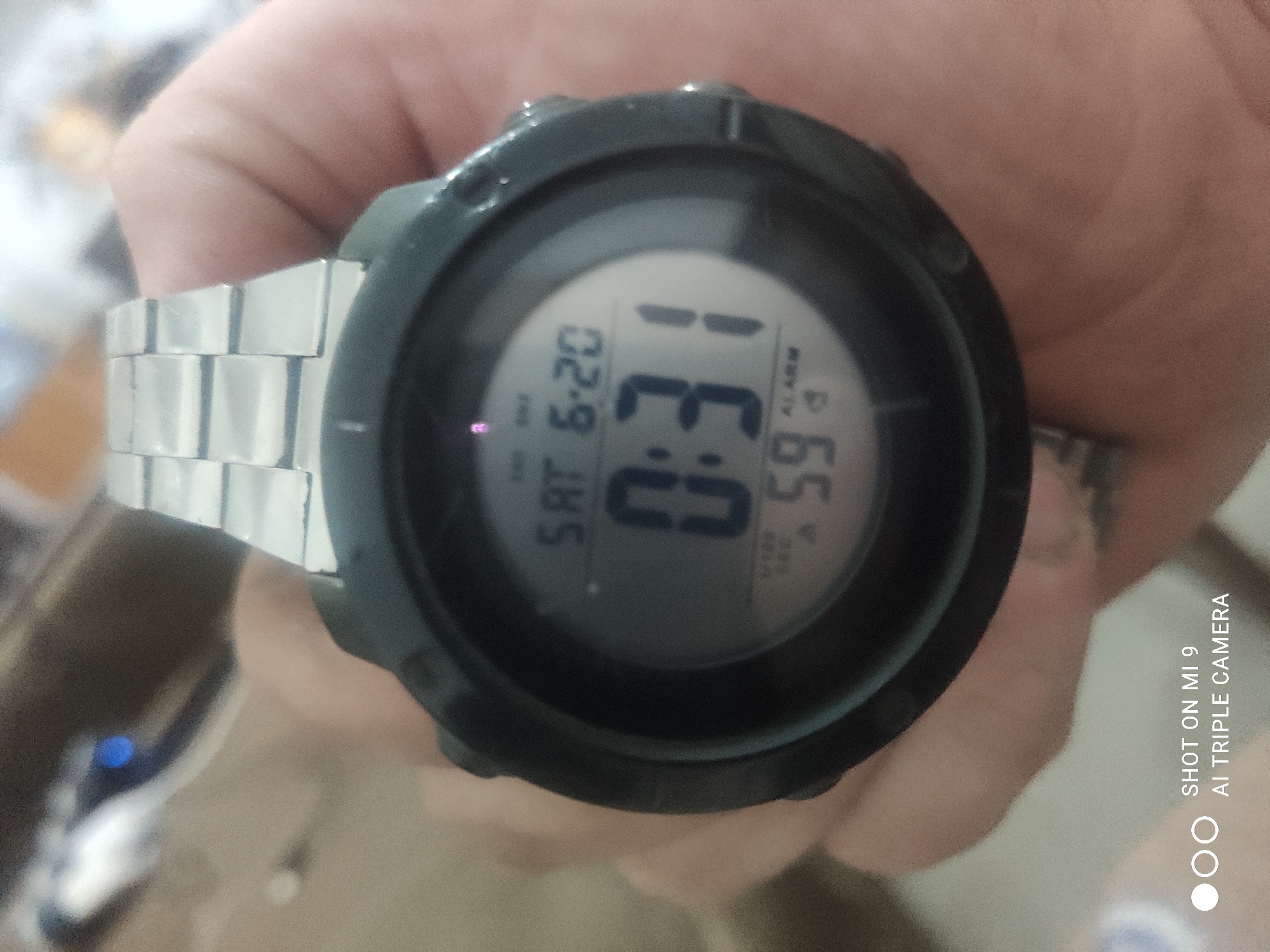 A digital watch with a silver band displays the time as 0:31 and the date as Saturday, June 20th. The watch face also shows "59" and the word "ALARM." The watch is on a person's wrist, with their skin visible around the watch. The background is blurred and appears to be indoors. There is a watermark in the bottom left corner that reads "SHOT ON MI 9 AI TRIPLE CAMERA."