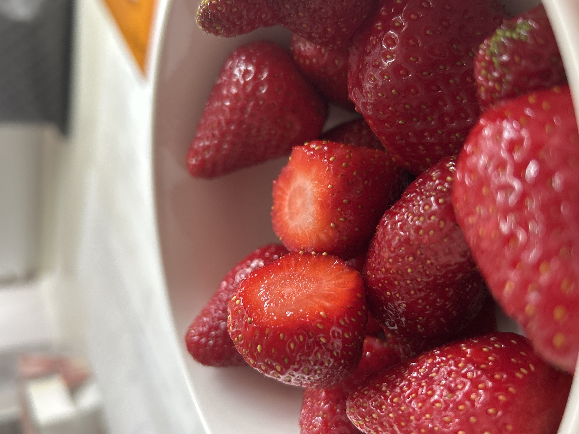The image shows a close-up of strawberries in a white bowl. The strawberries are red and appear fresh, with some cut in half. The background is blurred. The location in the city of Plovdiv, Bulgaria is unknown.