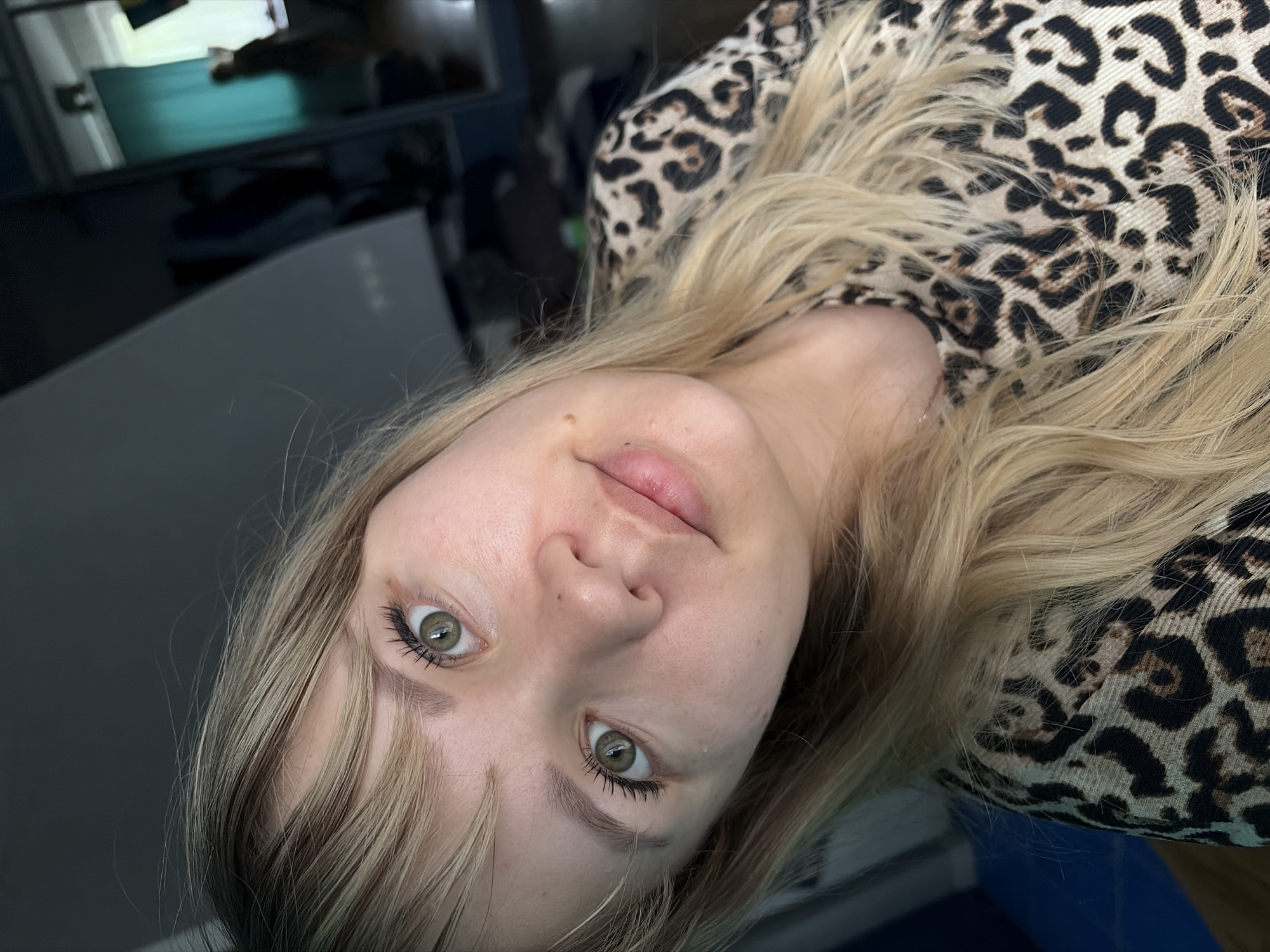 A close-up, angled headshot of a fair-skinned woman with blonde hair and hazel eyes. She is wearing a leopard print top. The background is out of focus, showing what appears to be furniture and room interior. There is no indication of the city of Chaikovsky, Russia.
