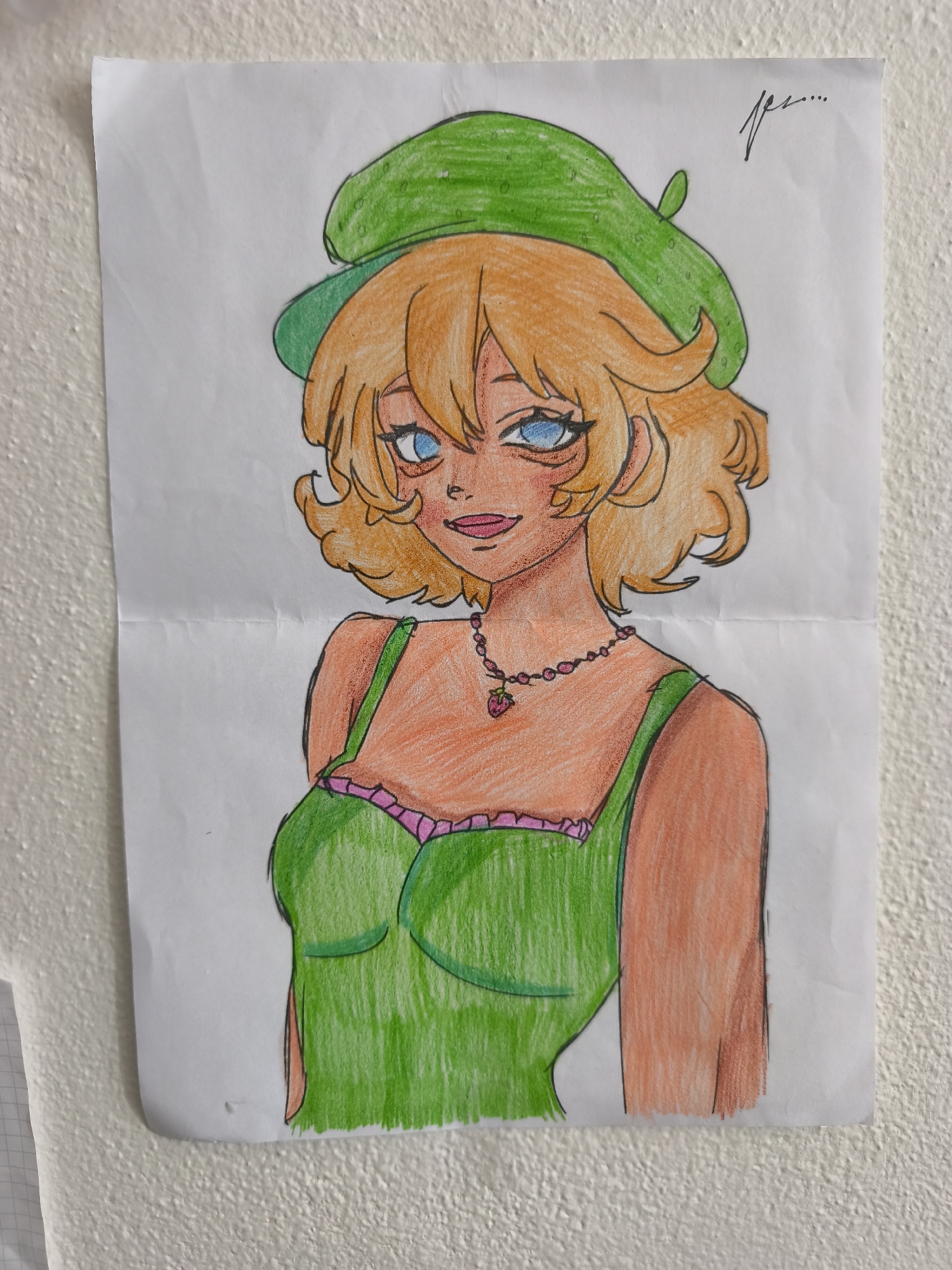 A hand-drawn colored pencil portrait of a young woman wearing a green beret and a green dress with pink trim is taped to a textured white wall. The woman has curly blonde hair, blue eyes, and is wearing a beaded necklace with a strawberry pendant. The drawing is on a sheet of white paper that appears to be folded horizontally. The wall is painted white and has a rough texture. The image is cropped to show the top half of the drawing and a portion of the wall. There is a faint handwritten signature in black ink in the upper right corner of the drawing, which appears to read "fpe....". The drawing is illuminated by natural light. The scene is indoors, in a room with a white wall. There are no other objects or people visible in the frame. The location is identified as Choceň, Czechia.