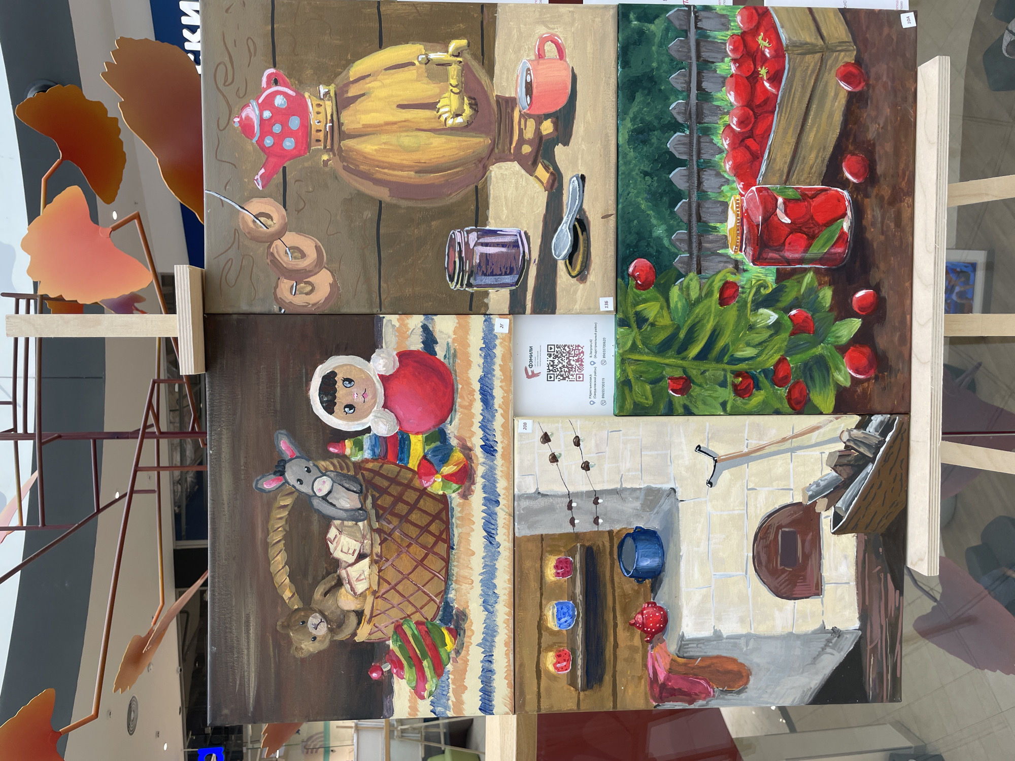 This media file displays a collection of four paintings arranged in a grid, likely an art exhibition or sale. The paintings are primarily still-life and folk art inspired.
The top-left painting depicts a traditional Russian samovar with a red teapot and steaming cup, alongside donuts and a jar of jam. The background is a muted brown, suggesting an indoor setting.
The top-right painting features a bountiful harvest of cherries. A wooden crate overflows with ripe cherries, a jar of preserved cherries sits on a wooden surface, and a cherry bush with lush green leaves and red fruit is in the foreground. The background shows a rustic wooden fence and greenery, hinting at an outdoor, possibly garden, setting.
The bottom-left painting showcases a playful scene with a matryoshka doll, a stuffed bear, and a toy rabbit peeking out of a woven basket. Wooden blocks with letters are scattered around, suggesting a child's play area. The background is a colorful striped pattern.
The bottom-right painting offers a glimpse into a traditional Russian stove (pech). The hearth with its opening is visible, along with logs of wood. A blue pot and red, yellow, and blue decorative spheres are placed nearby. A figure in a pink garment is seated on the floor in front of the stove. The scene suggests a cozy interior.
The overall impression is one of a folk art display celebrating traditional Russian themes and domestic life. Visible text includes numbers "208", "2г", "136", "10A", and Cyrillic text likely indicating a business name ("Фэмили") and contact information, including street names ("В. Засулич 42", "Р.Крестьянская"), a phone number ("89655700519", "89655700620"), and possible district names ("Свердловский район", "Индустриальный район"). The location context is identified as Perm, Russia.