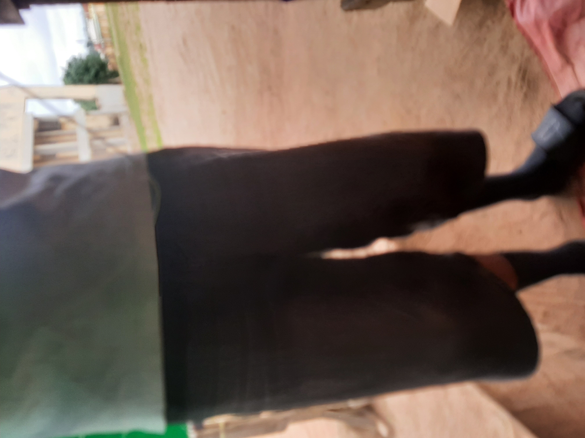 The image shows a person from the waist down, wearing dark shorts and dark socks. The person is standing on a dirt surface. In the background, there is a building that appears to be under construction or in disrepair, with concrete pillars and walls visible. There are also trees and a cloudy sky. The overall impression is that of an outdoor setting in a somewhat rural or developing area, possibly in the city of Ogbomosho, Nigeria. The image is blurry, making it difficult to discern fine details about the person or the environment.