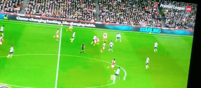 A soccer game is in progress. Players in red and white are facing off against players in white and black on a green field. Spectators fill the stands in the background. A banner reads "Game-changing banking. Life-changing habits." Another banner displays the word "STARLING". The broadcast shows "Premier League LIVE" in the upper right corner.