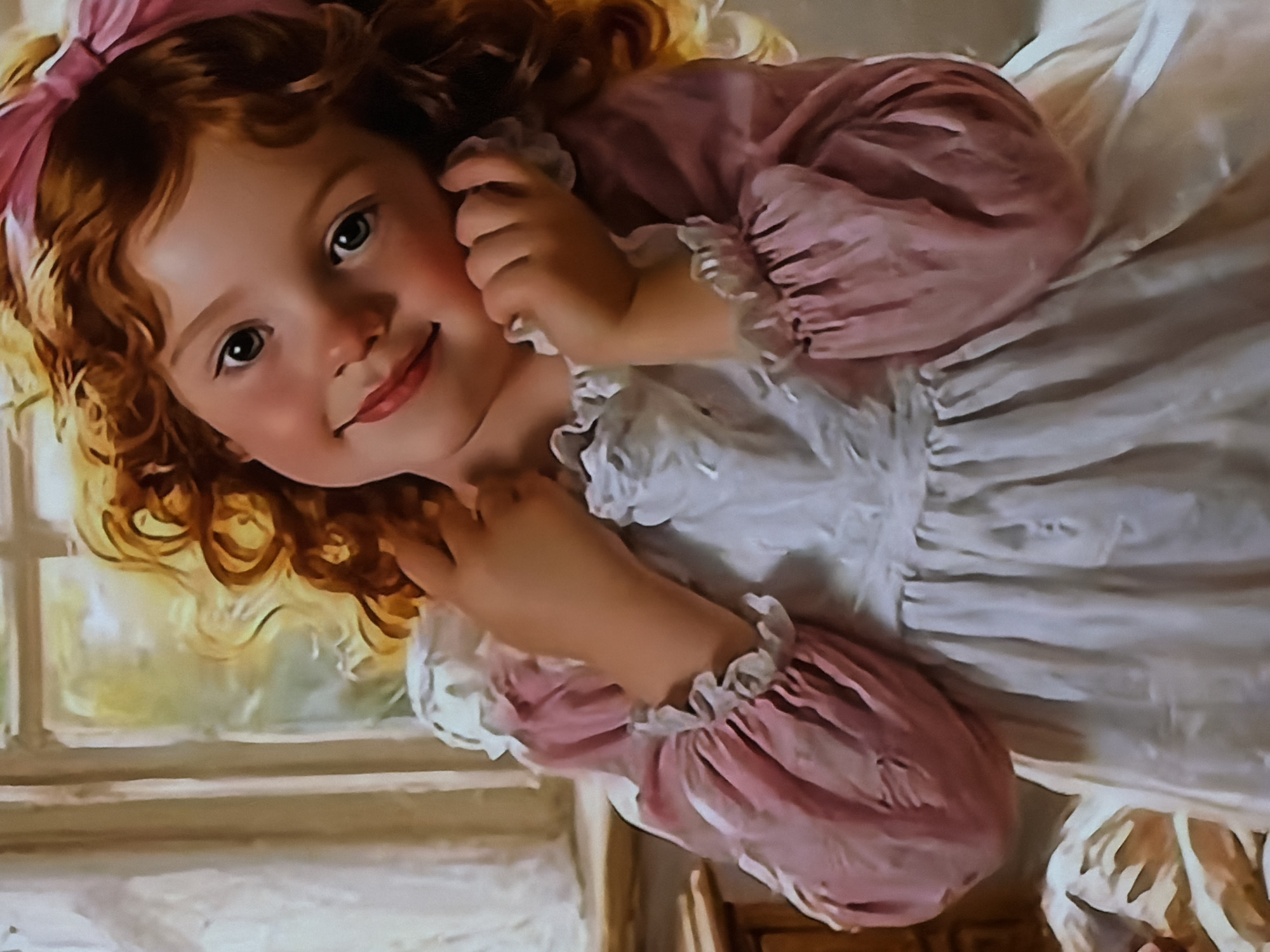 The media file is an artistic rendition, likely a painting or digital art in a painterly style, depicting a young girl. She has striking red or auburn curly hair, adorned with a soft pink bow on the top of her head. The girl is seen from a slightly elevated perspective, seemingly lying down or reclining, with her upper body and head angled towards the viewer. She wears a white dress with ruffled cuffs and puffy sleeves in a soft pink hue. Her complexion is fair, with rosy cheeks.
The girl's expression is gentle and endearing, with a subtle smile playing on her lips. Her dark eyes look directly at the viewer, conveying a sense of innocence and warmth. Her small hands are positioned near her face, one resting gently against her cheek or ear, adding to her charming demeanor.
The background suggests an indoor setting, with a soft, diffused light emanating from what appears to be a window on the left side of the frame, hinting at daytime. The overall ambiance is soft and bright, creating a serene atmosphere. No specific objects beyond the girl and hints of a window frame are clearly distinguishable. There is no visible text within the image. The emotional tone is sweet and innocent. The given location context for this image is Sofiivska Borshchahivka, Ukraine.