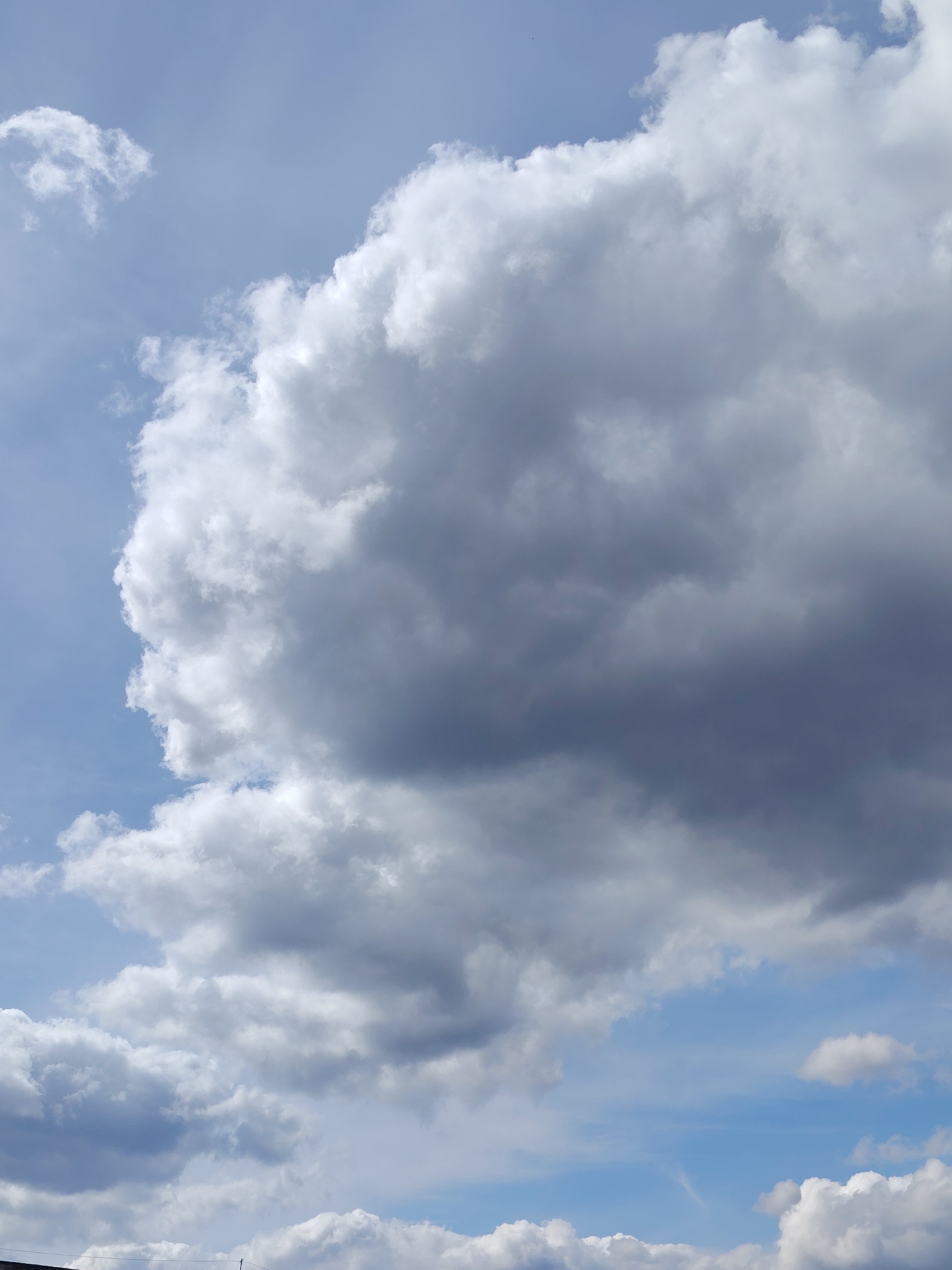 The image shows a view of the sky with various cumulus clouds of different sizes and densities. The sky is mostly light blue, with some areas appearing brighter and others darker due to the cloud cover. The clouds range in color from bright white to shades of gray. The image does not depict any features suggesting it was taken in Noviy, Russia, and there is no evidence of people, subjects, objects, actions, or interactions within the frame.