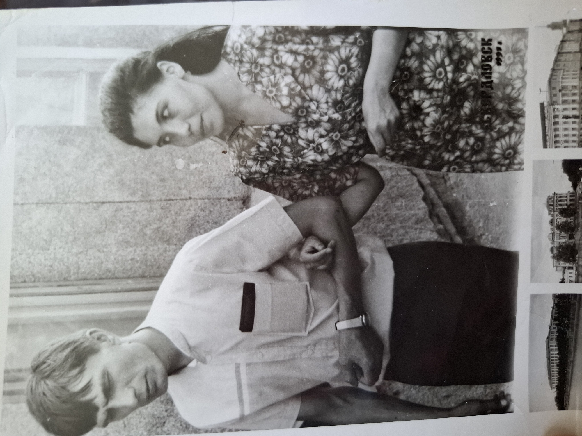 A black and white photo shows a man and a woman standing outdoors. The man is wearing a light-colored short-sleeved shirt with what appears to be a pocket on the left breast, dark trousers, and a watch on his left wrist. The woman is wearing a floral-patterned dress. Both are looking towards the camera. Next to them on the right side of the image is a series of smaller photographs showing what appear to be buildings. Text in Russian, possibly "Амзя 1991", is also visible next to the woman.