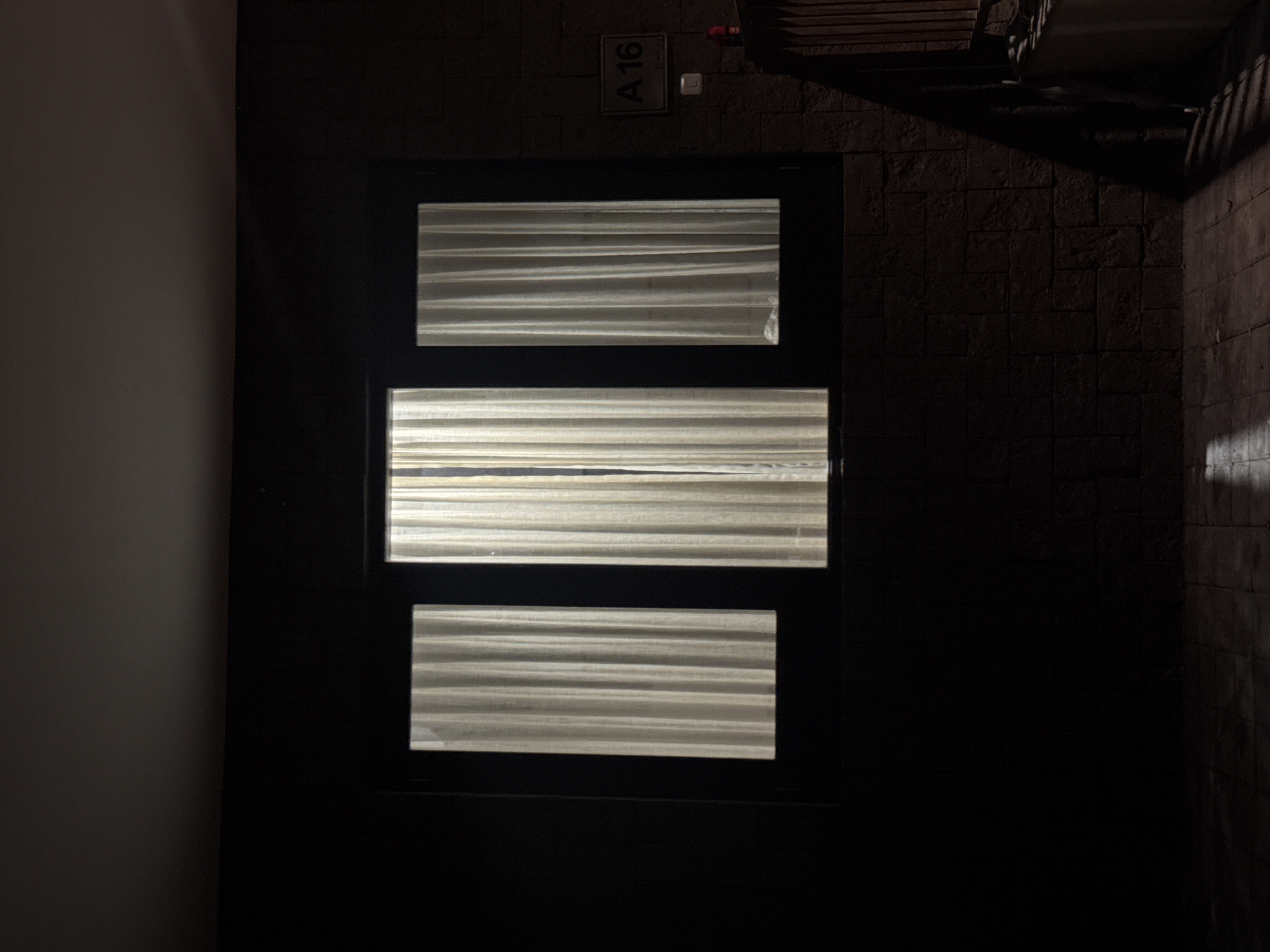 A dark doorway with three horizontal glass panes stands against a brick wall. "A 16" is printed on a small sign above the doorway. The location is Kuta Selatan, Indonesia.