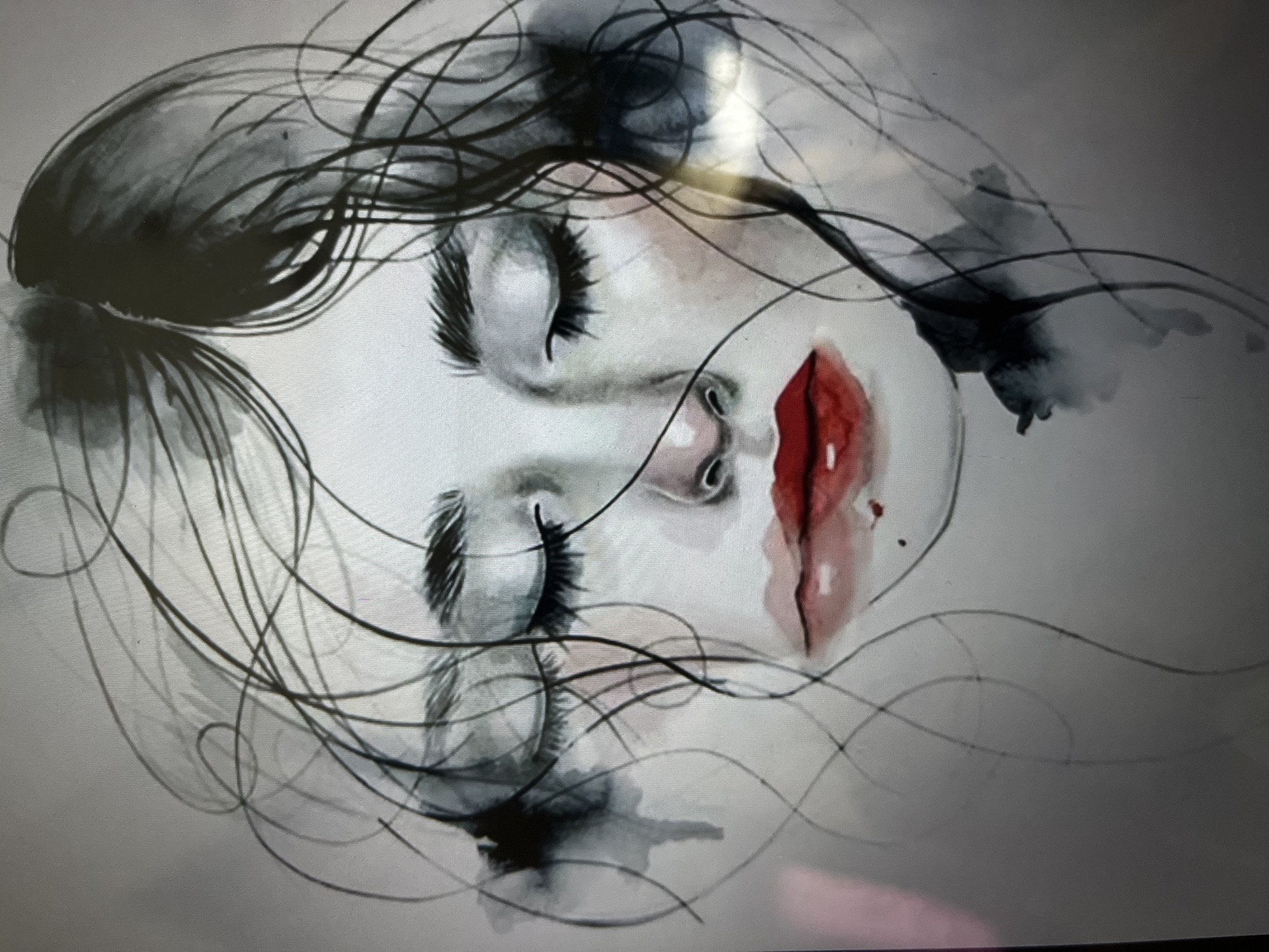 The image is a close-up, waist-up watercolor painting of a young woman's face, with her eyes closed. Her hair is dark and appears to be messy, with thin strands framing her face. Her eyebrows are dark and sharply defined, and her eyelashes are long and thick. She has high cheekbones, and her nose is small and delicate. Her lips are full and painted a vibrant red, with a slight shine. There are subtle hints of pink blush on her cheeks. The background is a light gray, with some smudged black watercolor elements on either side of her face, giving the impression of a dark shadow or wisps of smoke. The overall style is painterly and somewhat abstract, with a focus on emotion conveyed through the closed eyes and the bold lip color. There is no indication of a specific city or location in the artwork itself.