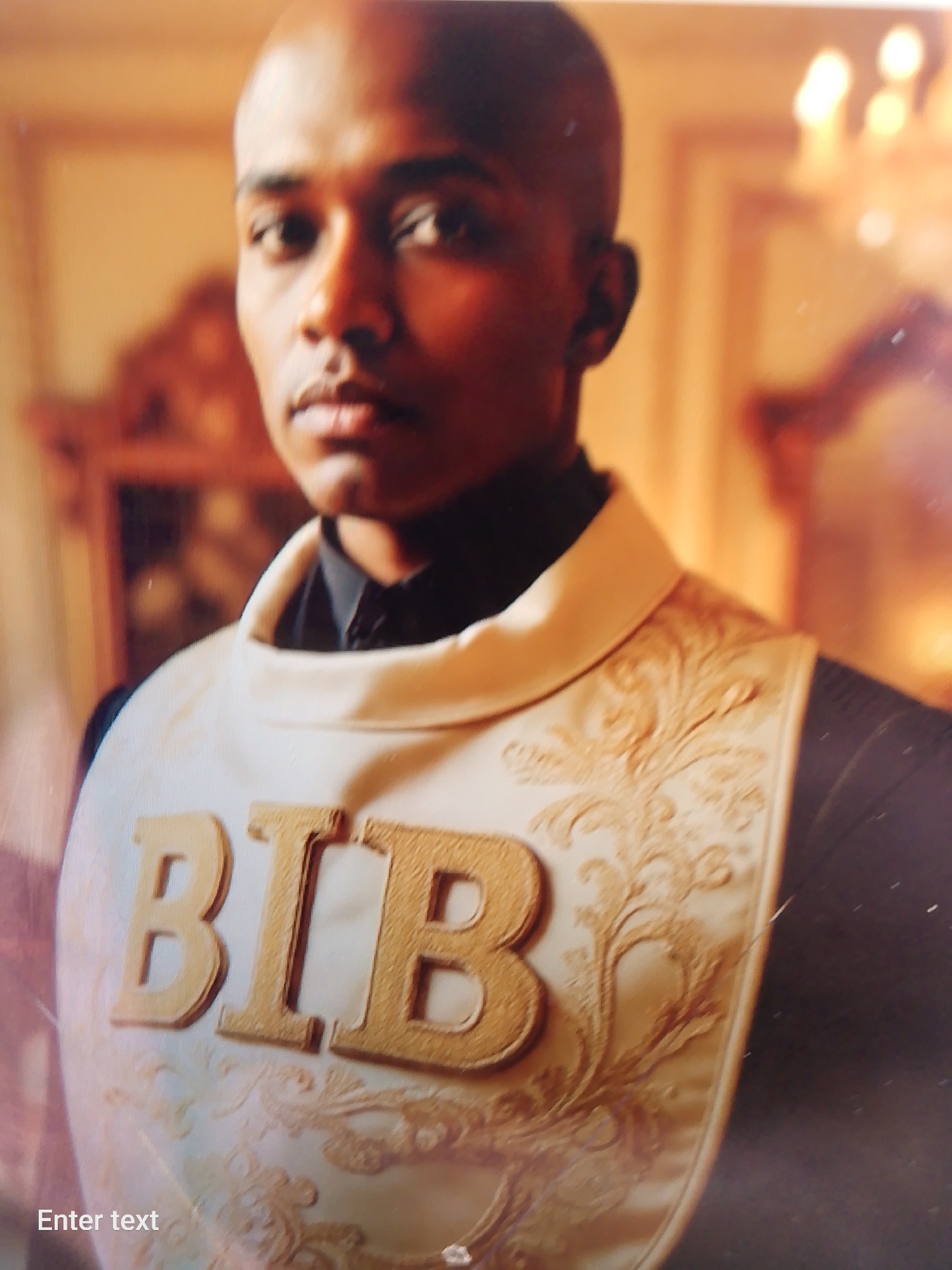 A close-up shot of a dark-skinned bald man wearing a bib with the letters "BIB" in gold. The bib is light-colored with an ornate design. The man is wearing a black shirt or jacket. The background is blurry, featuring what appears to be a framed mirror and a chandelier. There is no clear indication that this is in Adankolo, Nigeria.