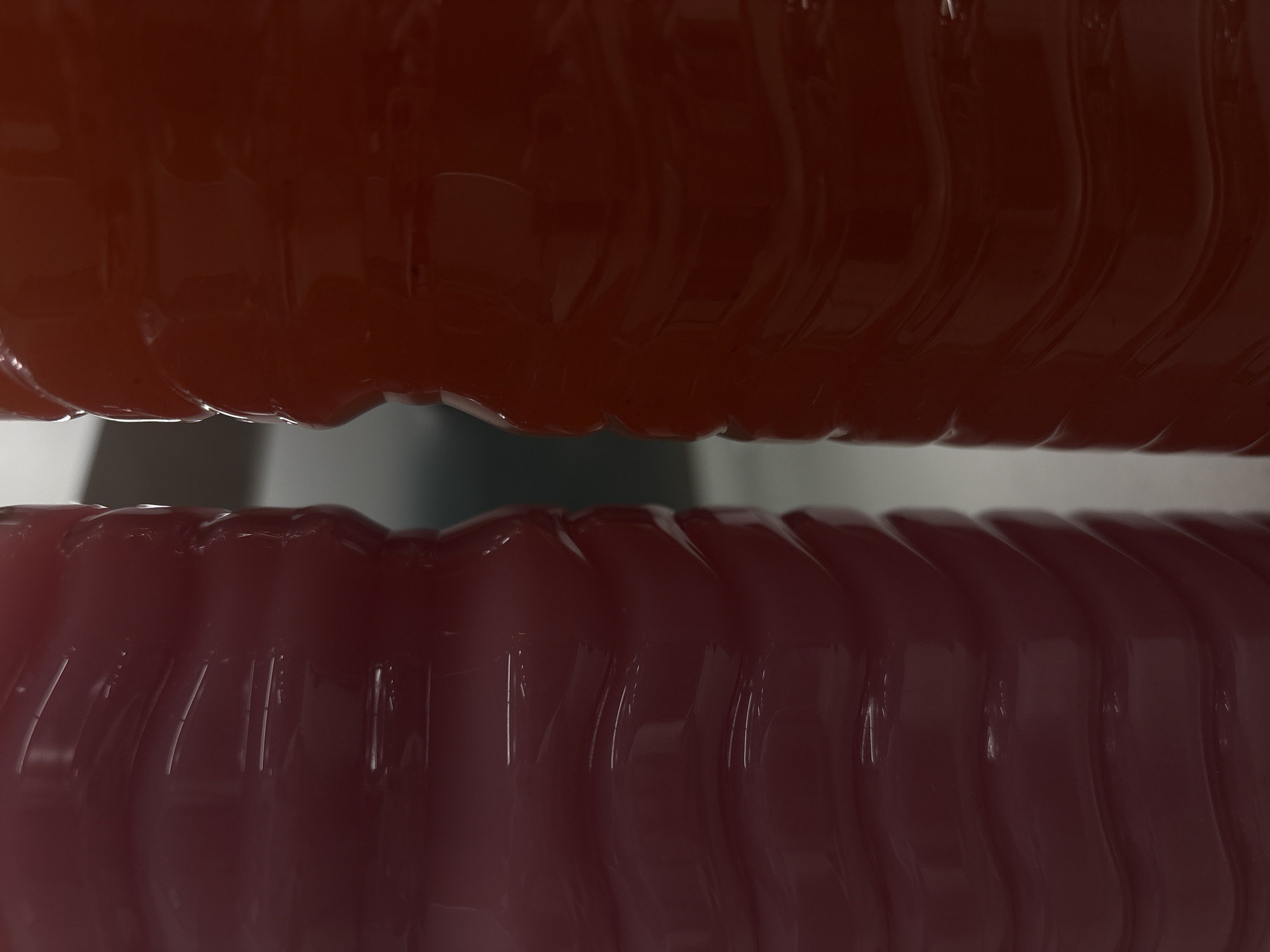 Two translucent, ribbed objects, appearing to be plastic bottles, are positioned closely together in the foreground. The top object is a deep reddish-brown, while the bottom is a lighter shade of reddish-pink. Both have a shiny, wet appearance. The background is out of focus, showing muted shades of gray and white. The scene's location in Puebla, Mexico is not discernible from the image alone.