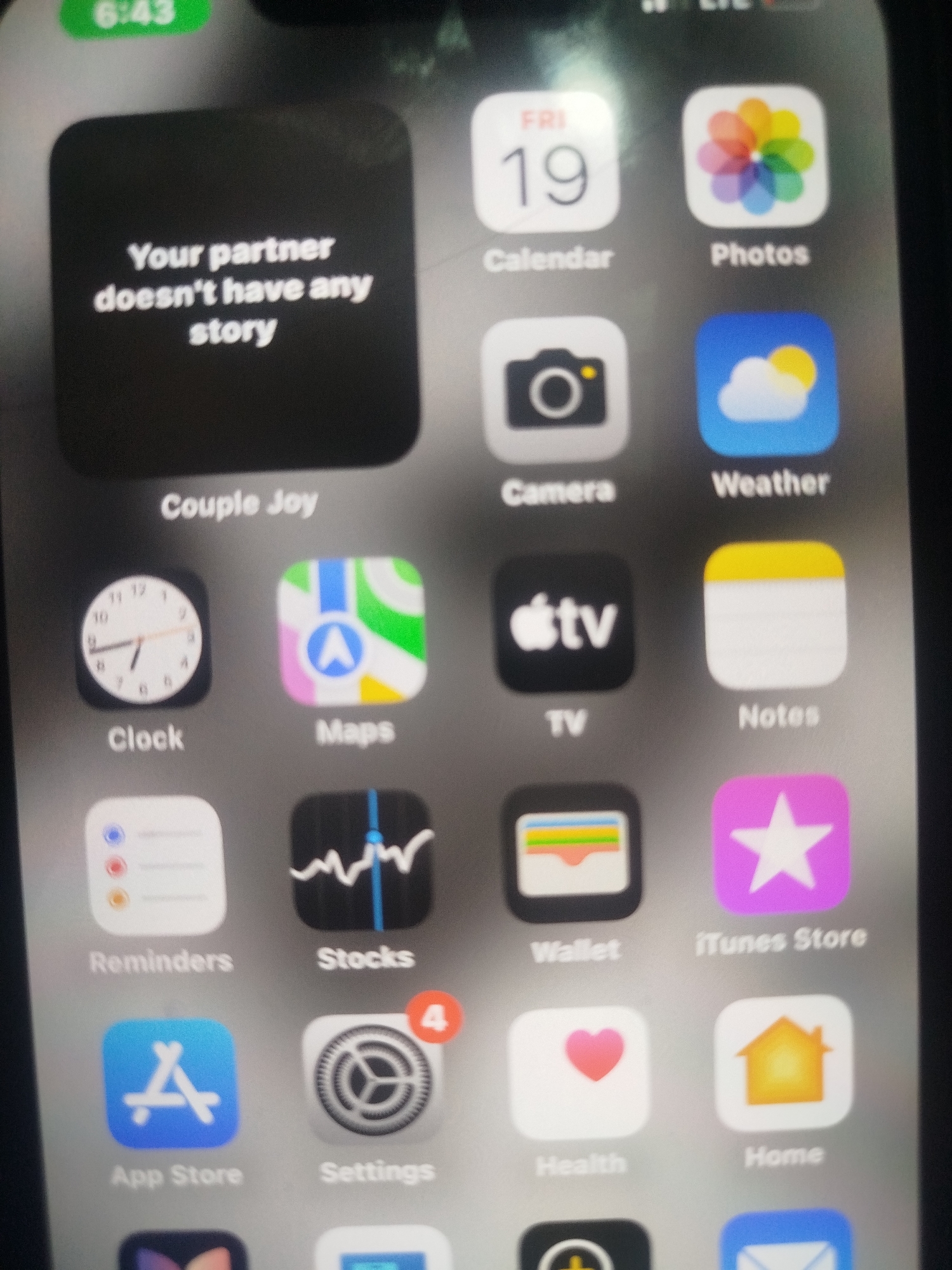 An iPhone screen displays a grid of app icons. The top left corner shows the time "6:43" in a green bar. A large black square icon on the left has white text that reads "Your partner doesn't have any story". Below this, the text "Couple Joy" is visible. The rest of the screen is filled with standard iOS app icons arranged in rows, including Calendar, Photos, Camera, Weather, Clock, Maps, TV, Notes, Reminders, Stocks, Wallet, iTunes Store, App Store, Settings, Health, and Home. Many of these icons have their corresponding text labels below them. The image appears to be a photograph taken of the phone screen, with some blurriness. There are no people or identifiable locations in the image.