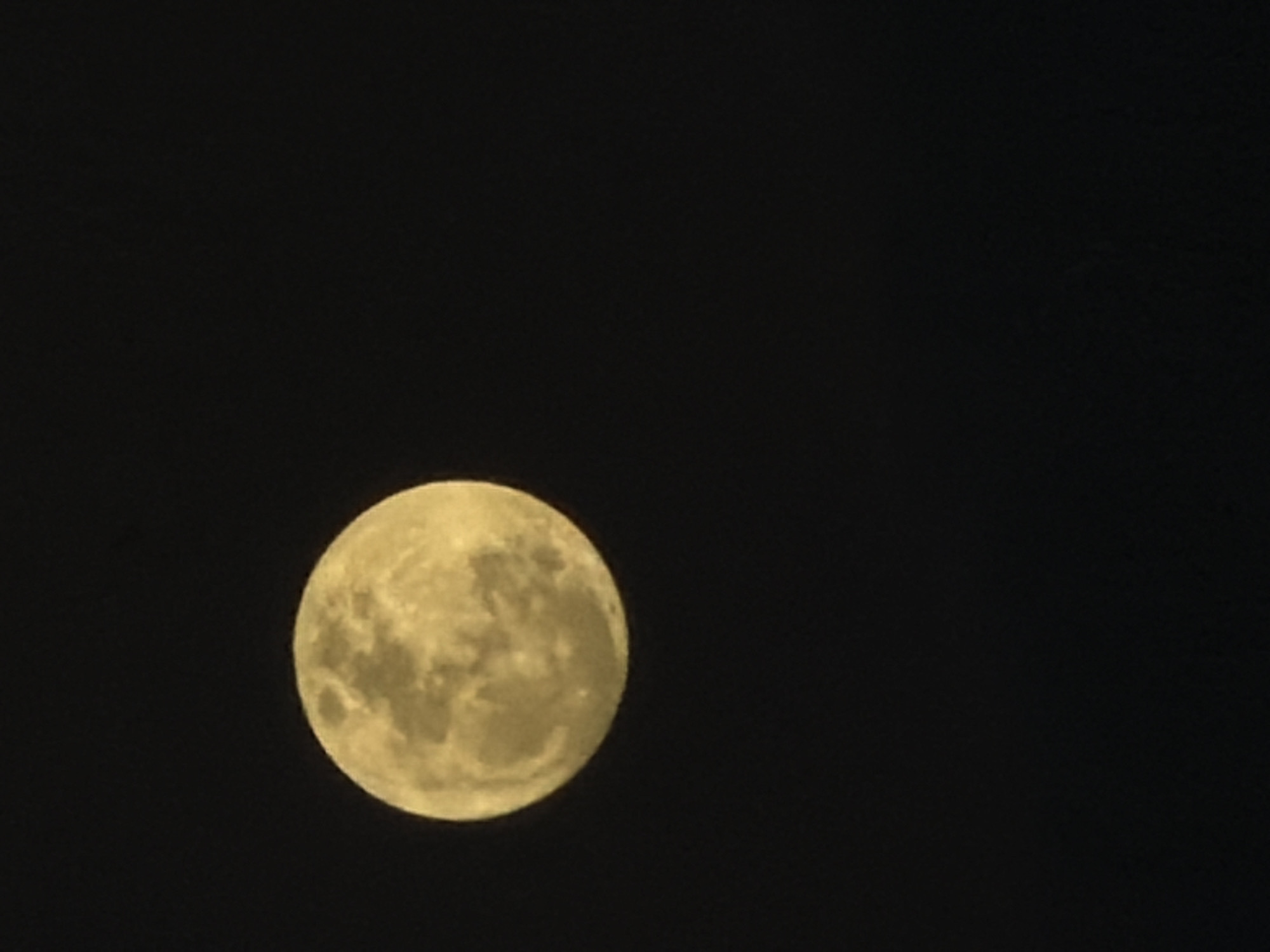 A full moon is visible in a dark, clear sky. The moon is illuminated and appears yellowish-white, with visible craters and surface features. The background is entirely black, suggesting nighttime and a lack of light pollution or other celestial objects. There is no indication of a specific location in North Kuta, Indonesia, or any human presence.