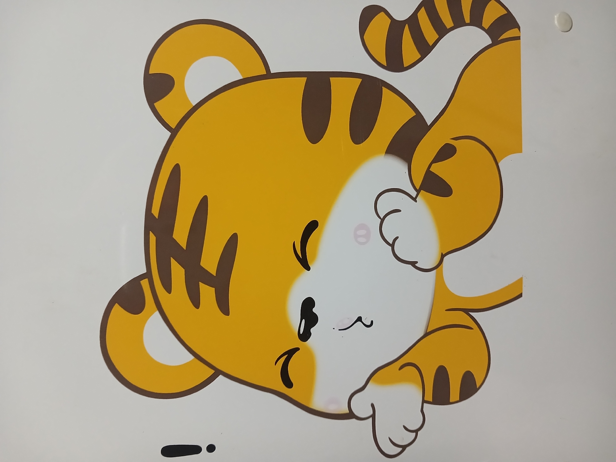 A cartoon drawing of a tiger cub with yellow and brown stripes is shown against a white background. The tiger cub has its eyes closed and its cheeks are rosy pink. Its mouth is puckered as if it is blowing a kiss, and its paws are held up to its face. To the left of the tiger cub is a black exclamation mark. The image appears to be a sticker or decal. The context of Randuagung, Indonesia is not discernible from the image itself.