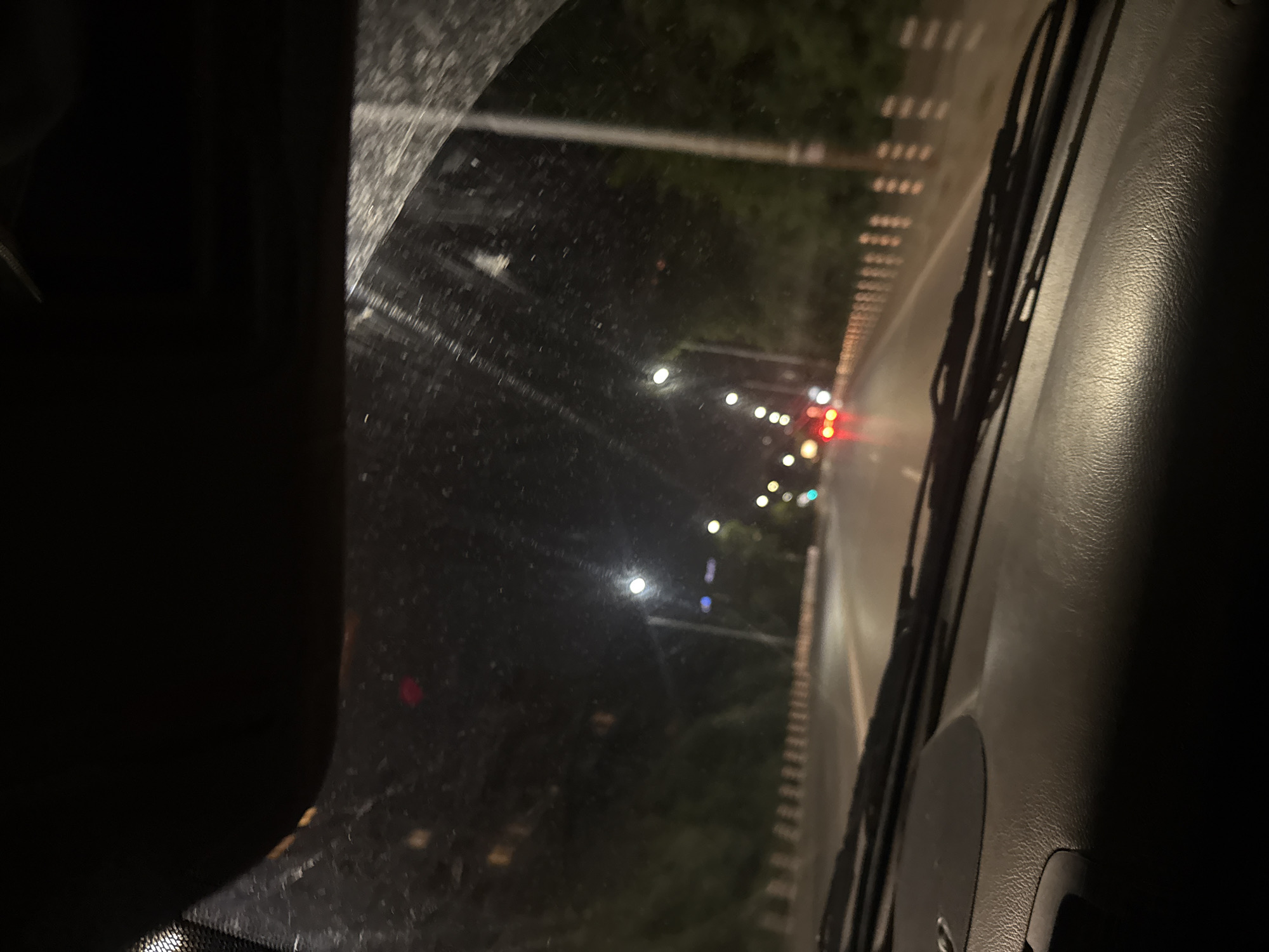 A nighttime view from inside a car driving on a road. There are other cars and streetlights visible in the distance. Rain or condensation obscures the windshield. The vehicle appears to be on a city road at night, possibly in Sofia, Bulgaria. Exact location details from the image are not possible.