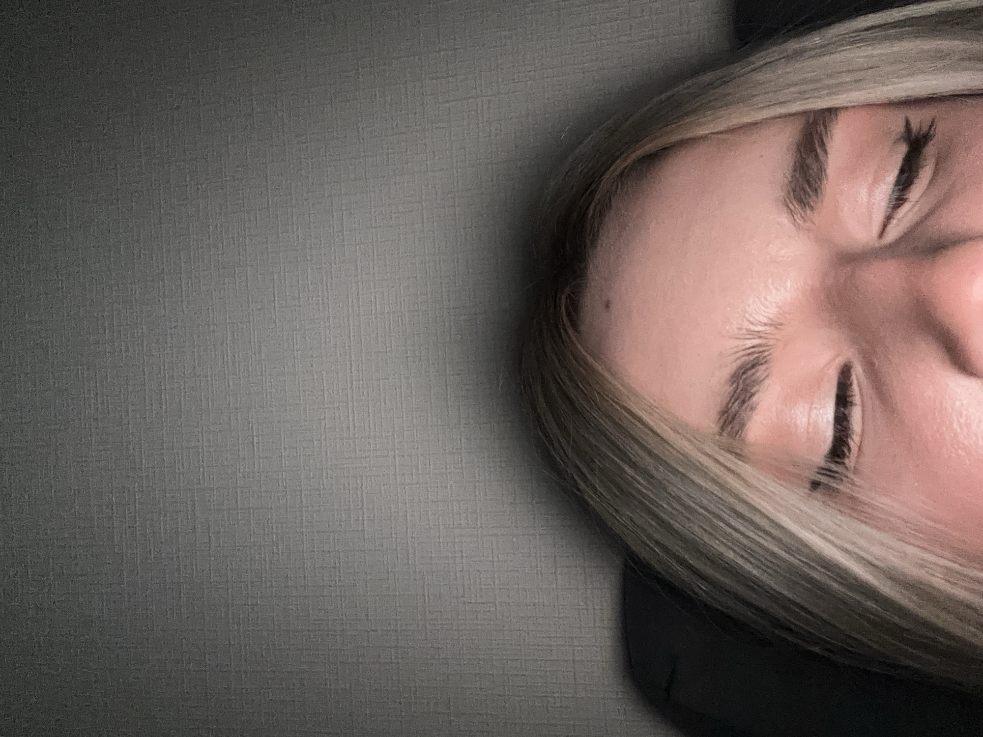 A close-up image shows the right portion of a person's face against a gray textured background. The person has light-colored hair and closed eyes. The background occupies roughly half of the frame. The image does not depict a location in the city of Vsevolozhsk, Russia.