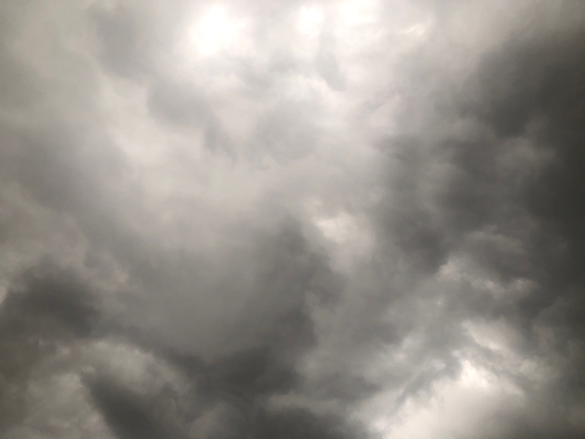 The image displays a sky filled with dark, ominous clouds, suggesting an impending storm. The lighting is dim, with patches of brighter sky peeking through the dense cloud cover, indicating diffused sunlight. There are no people, subjects, or objects visible in the frame, nor are there any discernible actions or interactions taking place. The environment is solely characterized by the turbulent atmospheric conditions. There is no information about the specific location within Rigasa, Nigeria, that can be determined from the image itself.