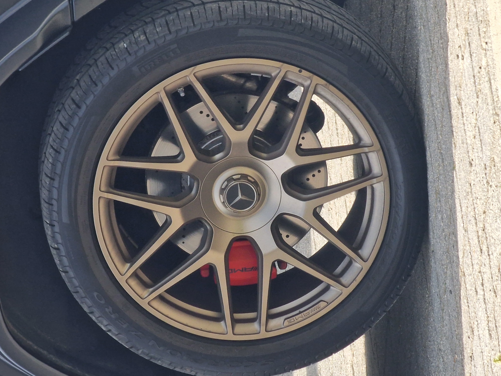 The image shows a close-up of a car wheel. The wheel is a complex design with multiple spokes and a gold-colored finish. Behind the spokes, the car's braking system is visible, including a red brake caliper. The tire surrounding the wheel is black and appears to be high-performance. There are no people visible in the image. The setting is ambiguous and cannot be conclusively determined to be Witton Gilbert, United Kingdom, without additional visual or contextual information. The environment appears to be outdoors due to the available lighting.