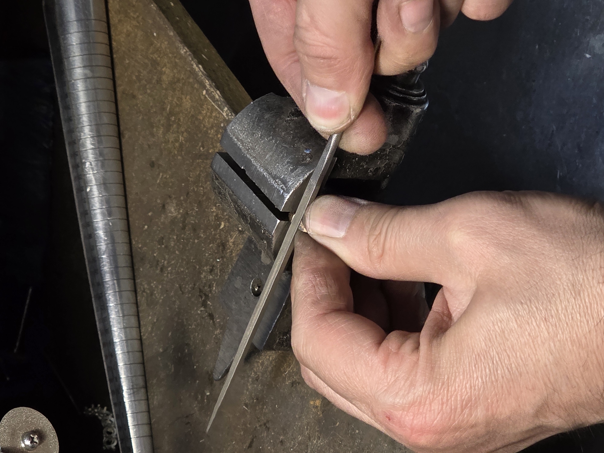 A close-up shot shows a pair of hands filing a small metal object held in a vise. The background consists of a workbench and some tools, including a ring mandrel with size markings. The scene appears to be in a workshop or studio. There is no information in the image that suggests a specific location in Kazan, Russia.