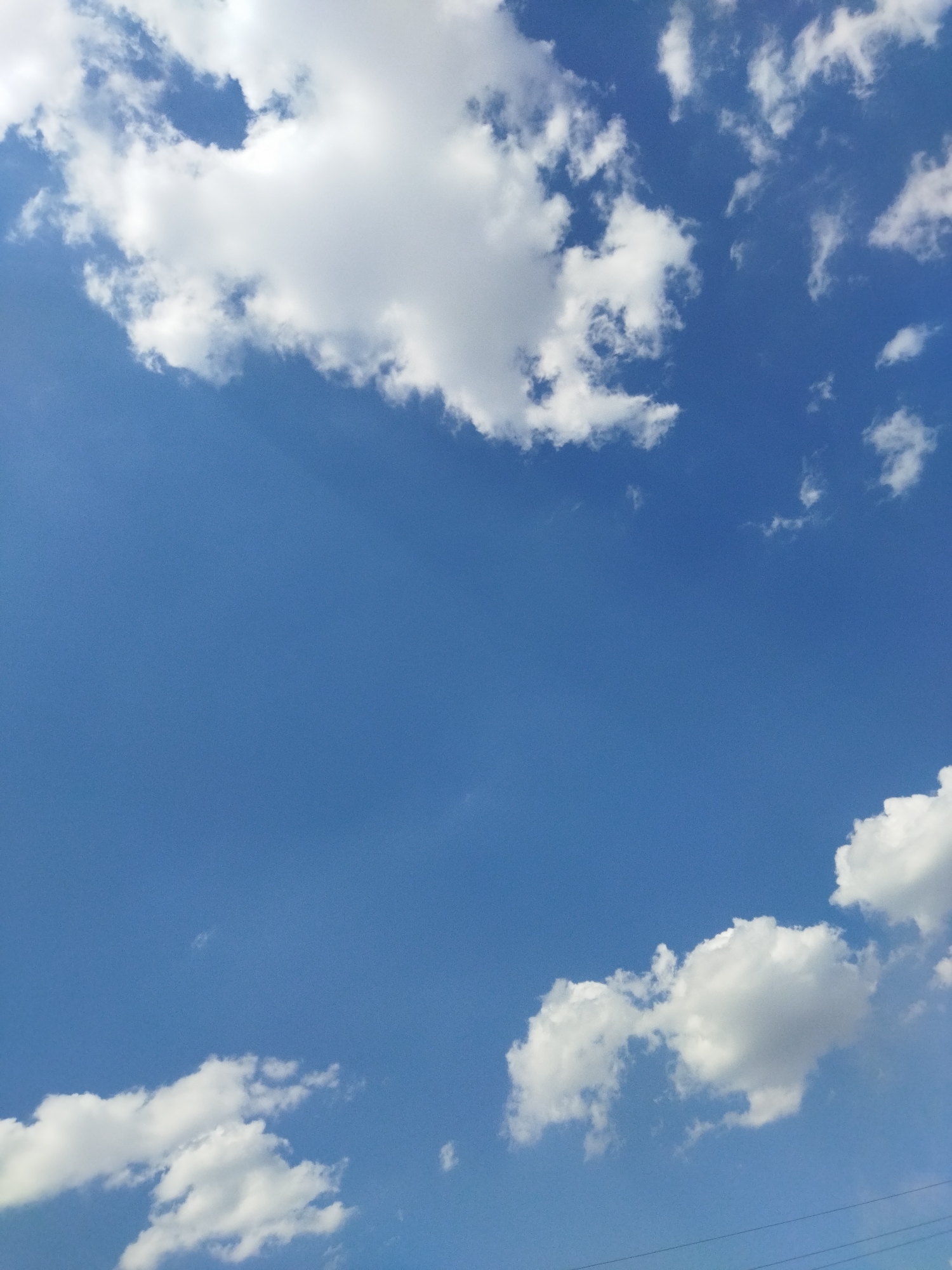The image captures a clear blue sky filled with scattered white cumulus clouds. The clouds are illuminated by sunlight, creating bright white patches against the vibrant blue backdrop. There are no visible people, buildings, or specific landmarks that would indicate a precise location within Astana, Kazakhstan. The scene is a natural outdoor environment dominated by the sky and clouds.
