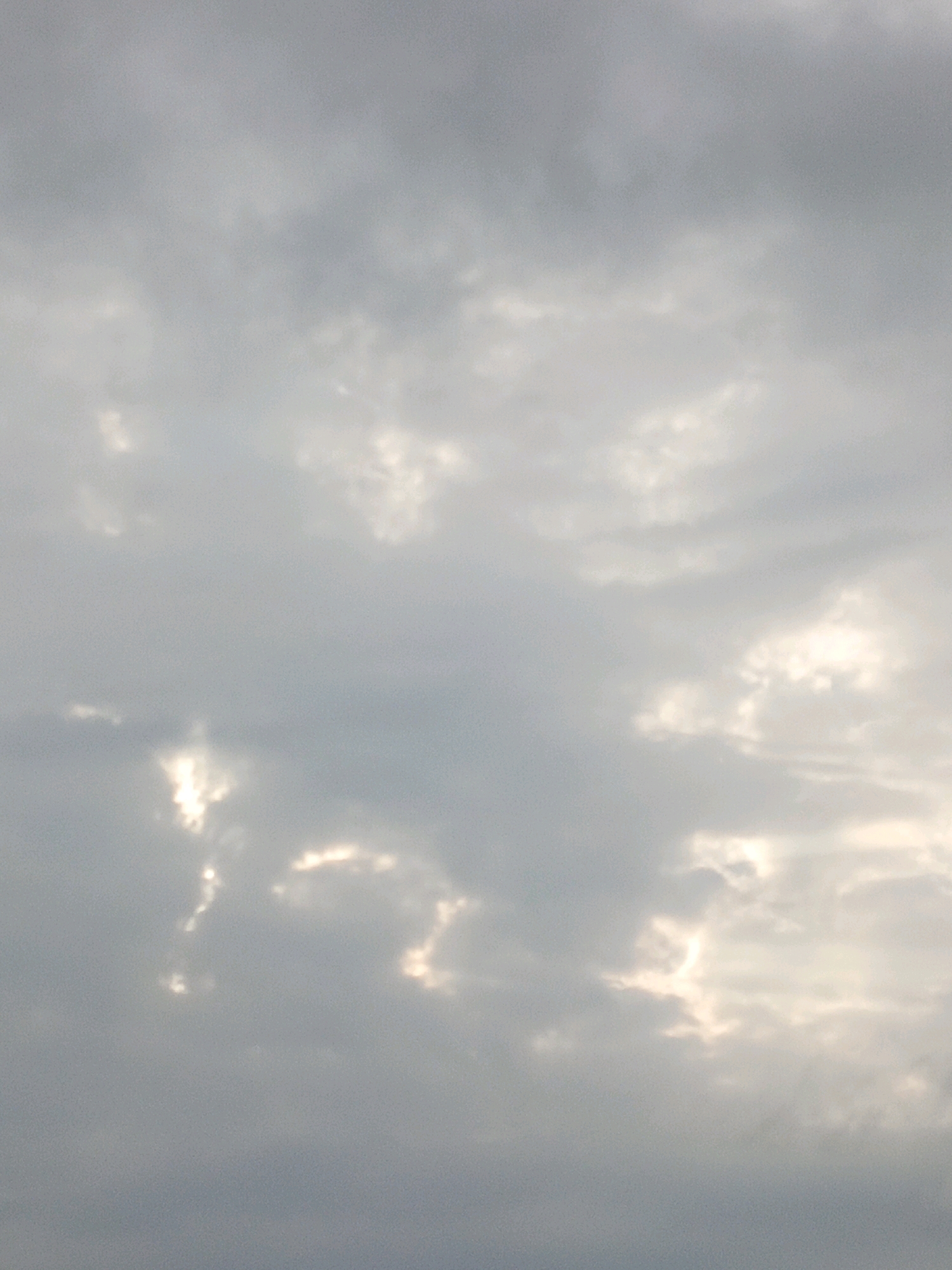 A cloudy sky is depicted in the image, with patches of sunlight breaking through. The clouds are various shades of gray and white, with some appearing denser than others. The sunlight creates bright spots and highlights on the cloud formations. The overall scene is atmospheric and somewhat subdued due to the cloud cover. The image was taken in Bulukumba, Indonesia.