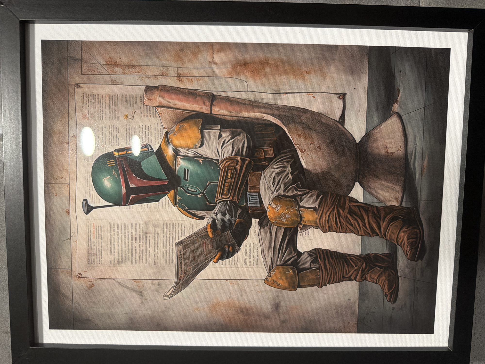 The media file presents a framed artwork depicting the Star Wars character Boba Fett. He is shown in his iconic Mandalorian armor, featuring a green and red helmet, yellow and green chest and shoulder plates, brown gauntlets, and a flowing cape. Boba Fett is positioned in a kneeling or crouching posture, leaning slightly to one side.
He holds an aged, folded document, resembling a newspaper or bounty poster, in his gloved hands, appearing to be examining its details. The background of the artwork is a textured, stylized surface, predominantly in muted tones of brown, gray, and beige. It incorporates indistinct blocks of printed text, akin to old newspaper pages or book excerpts, adding to its worn aesthetic. Rust-like stains and faded lines are visible throughout the background, suggesting a gritty, industrial, or aged environment.
The artwork has a painted or illustrated quality, with visible texture. It is enclosed within a simple black frame and a white mat, with reflections indicating it is under glass or a protective layer. The text within the background and on the document Boba Fett holds is too small and abstract to be legible, functioning more as a textural and atmospheric element within the composition.