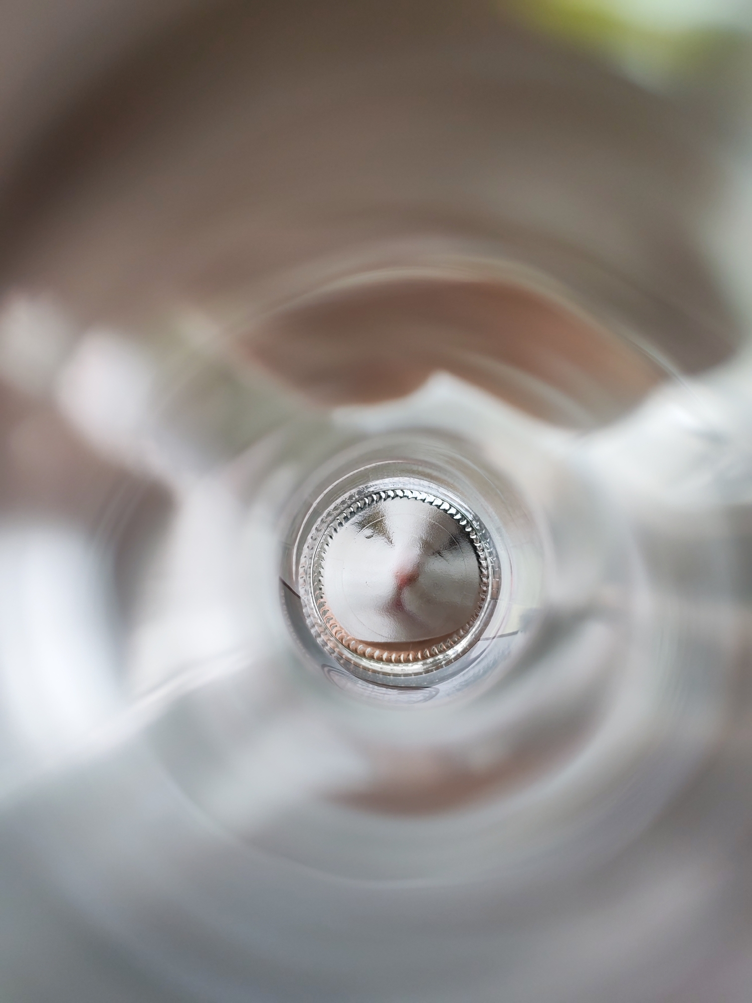 The image shows the inside of a clear glass bottle, looking towards the bottom. The base of the bottle is visible, with a textured edge. The surrounding environment is blurry and out of focus, with indistinct shapes and colors. There is no discernible information to indicate the location is Chaikovsky, Russia. No people, actions, or interactions are visible.