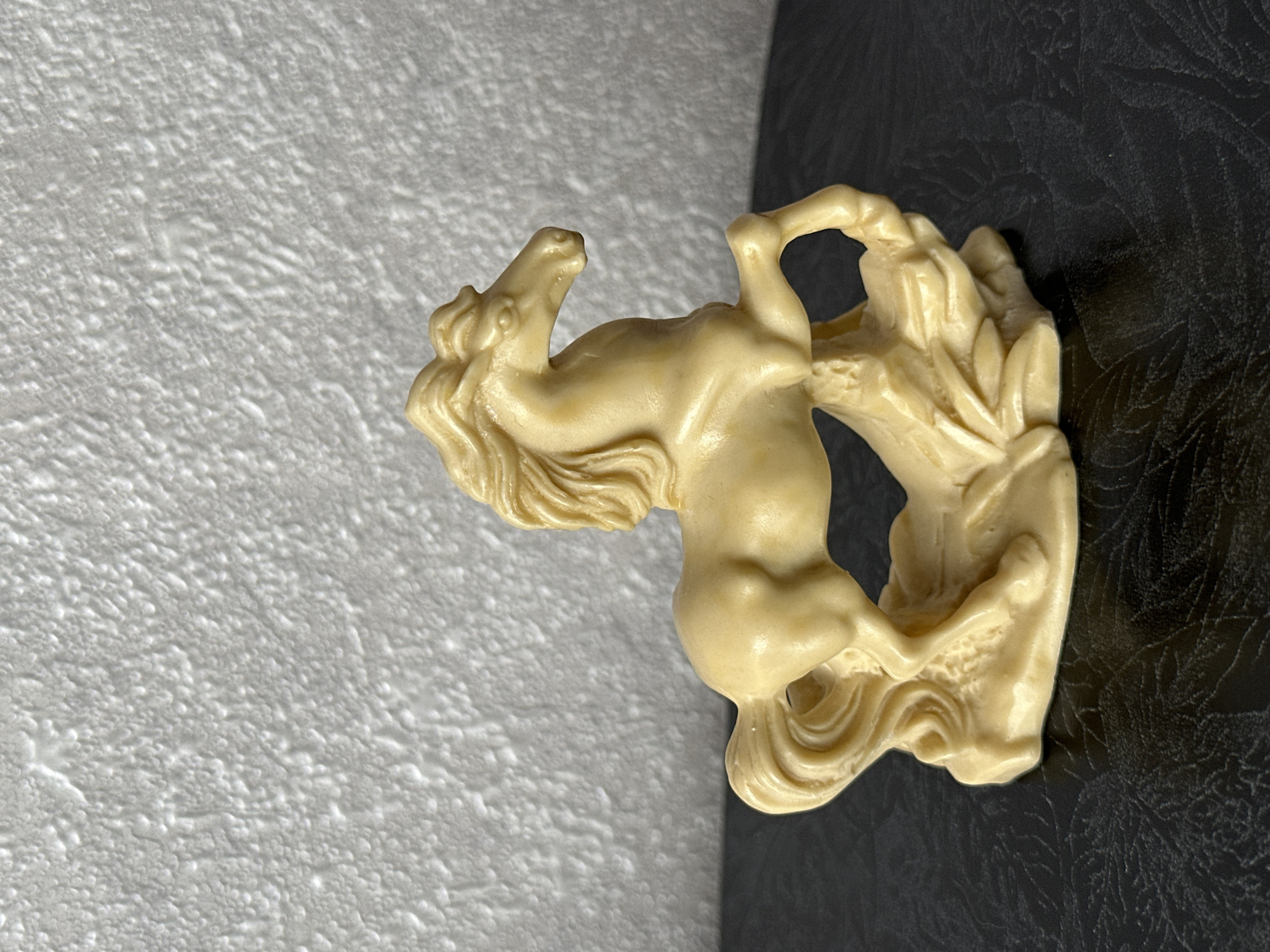 A light cream-colored figurine of a horse in a dynamic pose stands on a dark, textured surface. The horse is depicted with its front legs raised and its tail flowing. The background is a white, textured wall. The location is Energetik, Russia.