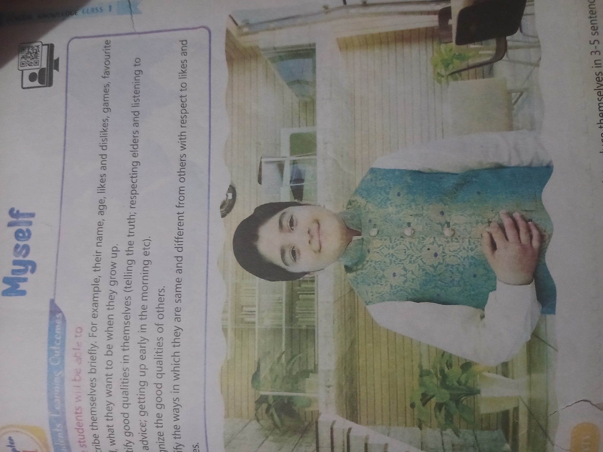 The image shows a page from a textbook with the title "Myself" prominently displayed. Below the title, a section titled "Students Learning Outcomes" outlines objectives related to self-description. The learning outcomes include describing oneself briefly, mentioning future aspirations, identifying good qualities in oneself and others, and recognizing similarities and differences with others.
A photograph of a young boy is placed in the lower half of the page. The boy is smiling and wearing a white shirt with a blue and gold patterned vest. He is positioned in front of a background that appears to be an indoor setting, possibly a room in a home or a school, with shelves containing books visible in the background.
There is no information in the image that suggests a specific location in Peshawar City Tehsil, Pakistan, or any other geographical context beyond what is implied by the textbook's content. The scene is a still image and does not depict any actions or interactions beyond the posed photograph of the boy. The overall presentation is that of educational material.