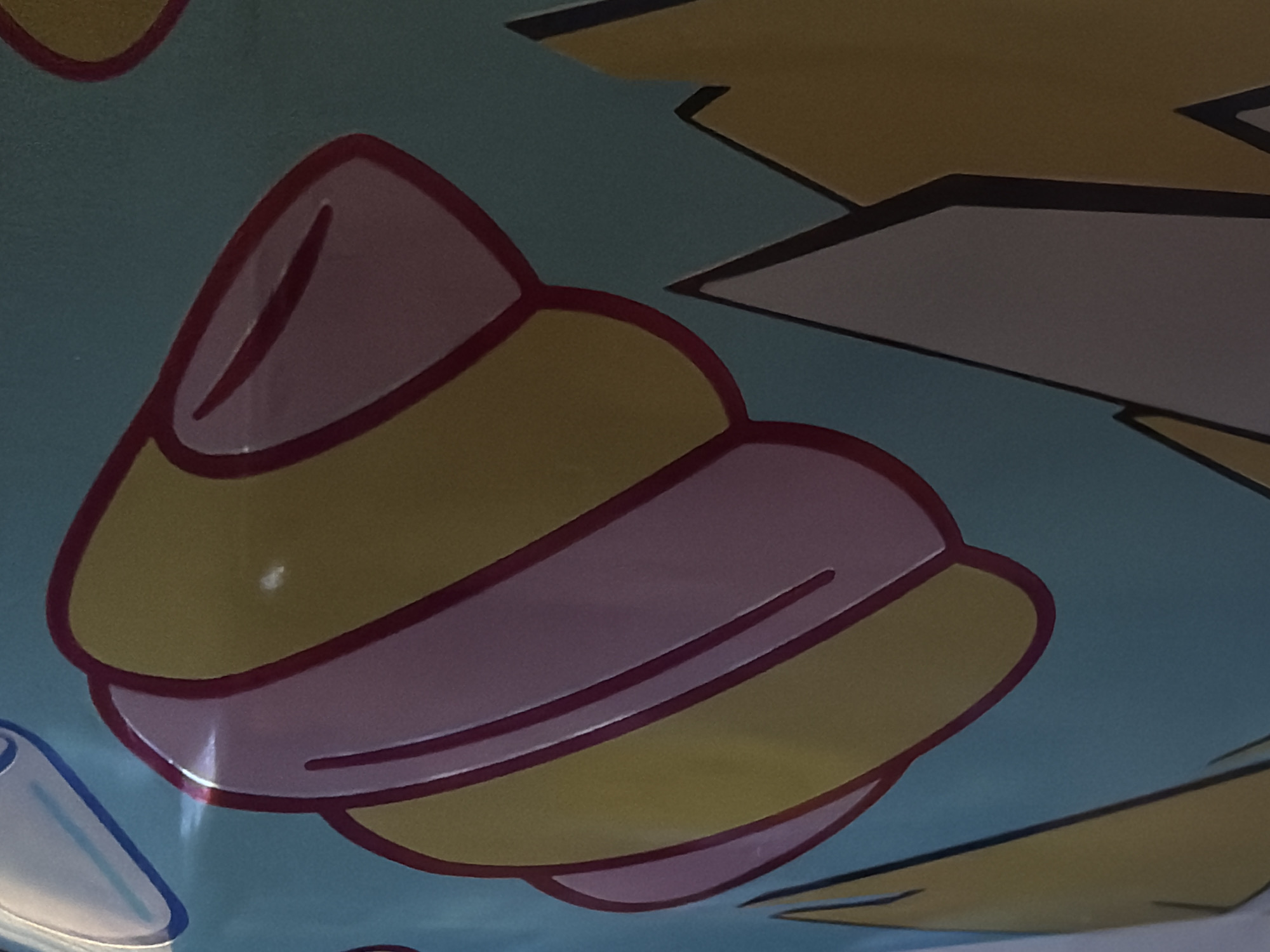 The image shows a close-up of a colorful illustration on a teal background. The illustration features rounded, abstract shapes in yellow and pink, outlined in dark red, resembling a stylized shell or a layered confection. In the lower right portion of the image, sharp, angular shapes in yellow and gray with dark outlines suggest a landscape or abstract mountain-like forms. The lighting suggests this is an indoor photograph, possibly of a printed material or artwork. The provided location of Дубрава-2 Снт, Russia is a rural settlement and does not provide specific visual context for the image itself.