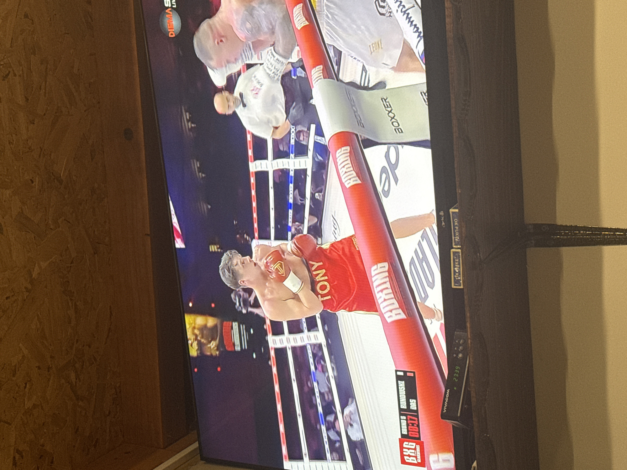 The image shows a television screen displaying a boxing match between Tony and Runowski, during round 6 with 0:17 on the clock. The TV is placed near a wall, and a VIVACOM box is visible next to the screen. The fight features two boxers in the ring, with a referee present. The event is sponsored by various brands including BOXER, de, BXG GLAVURTERS, and DIEMAS. The location is suggested to be connected to Prisovo, Bulgaria, possibly through the VIVACOM network, which is a Bulgarian telecommunications company.