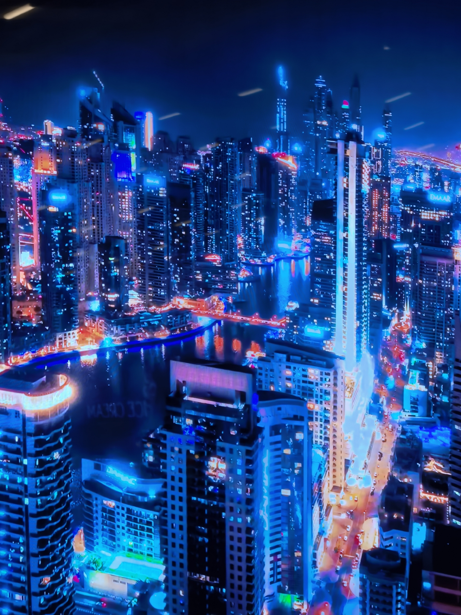 The image depicts a futuristic cityscape at night, characterized by a predominance of vibrant blue and purple neon lights illuminating towering skyscrapers. The architecture is modern and dense, with many buildings featuring sharp angles and reflective surfaces. A body of water, likely a canal or river, snakes through the city, reflecting the dazzling lights. Vehicles are visible on the roads below, appearing as streaks of light due to the long exposure or movement. The overall atmosphere is one of a technologically advanced metropolis. However, there is no indication that this scene is located in Fergana City, Uzbekistan. The architecture and lighting style are more commonly associated with major global cities known for their modern skylines.