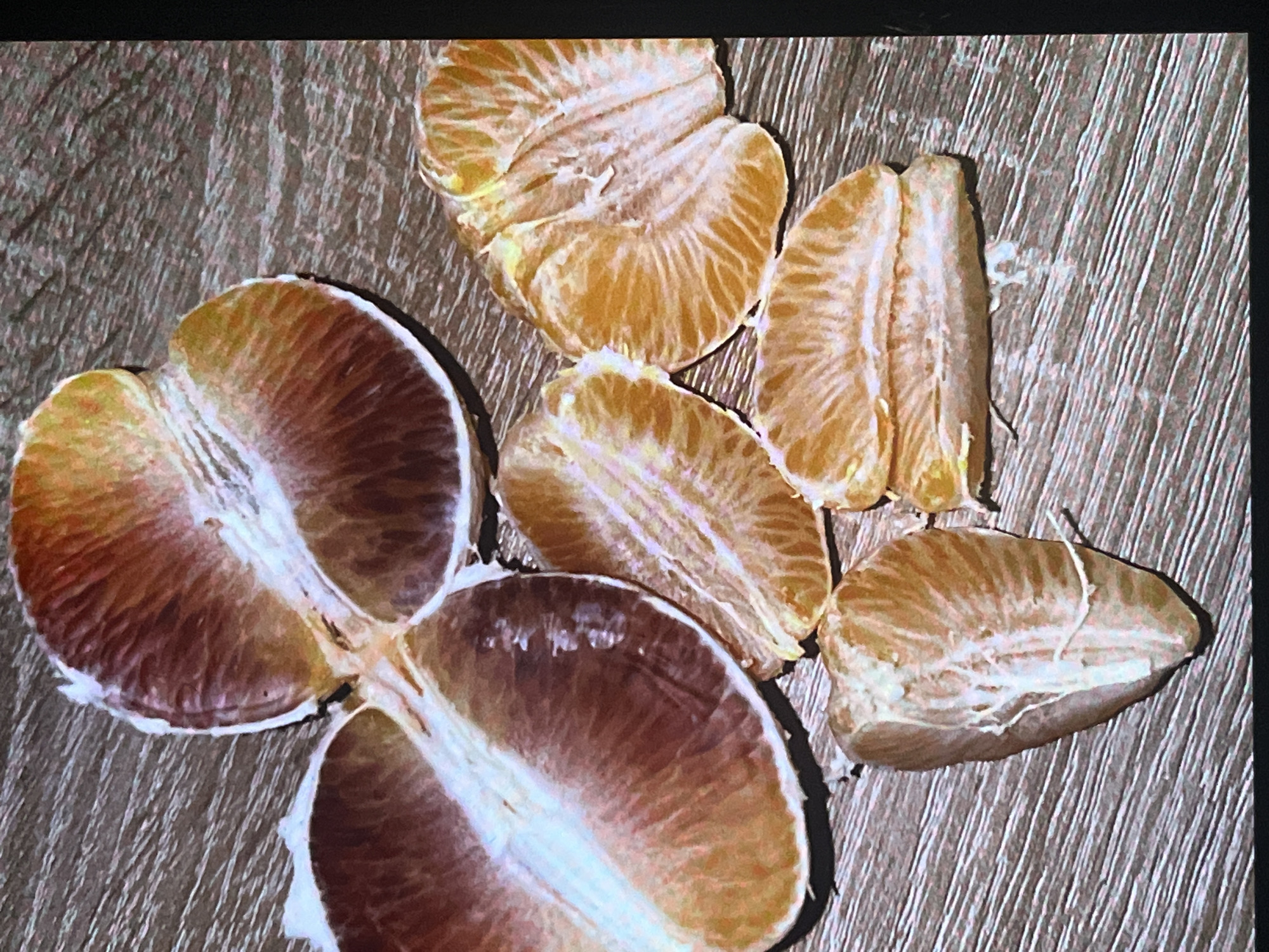 The image displays a close-up, overhead view of several peeled segments of a blood orange arranged on a wooden surface. The blood orange segments exhibit a rich, reddish-orange hue with some lighter, yellowish-white sections. Some segments are whole, while others appear to be portions of larger segments. The wooden surface has a visible grain pattern. The image is cropped and does not show any context outside of the fruit and the surface it rests on. There is no indication of the location in Ferdinandshof, Germany.