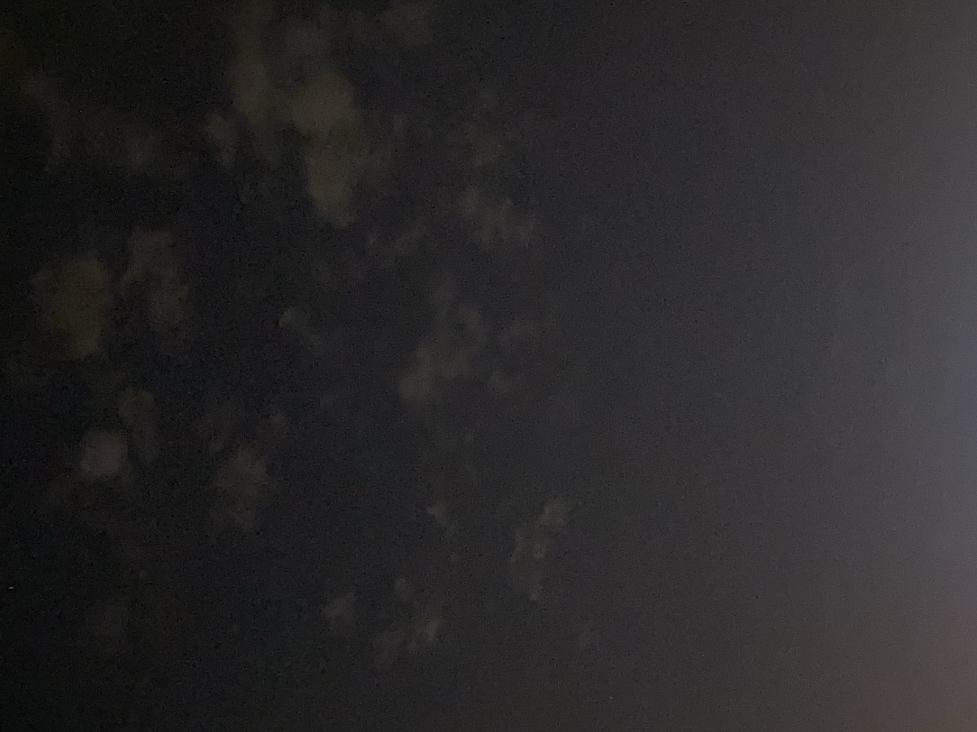 The image displays a dark, cloudy night sky with faint celestial bodies. The lower portion of the image shows a gradient of light, suggesting a distant light source, possibly artificial. The scene is devoid of any discernible landmarks or urban features that would definitively place it within Iași, Romania. The overall impression is of a typical night sky over an unspecified location.
