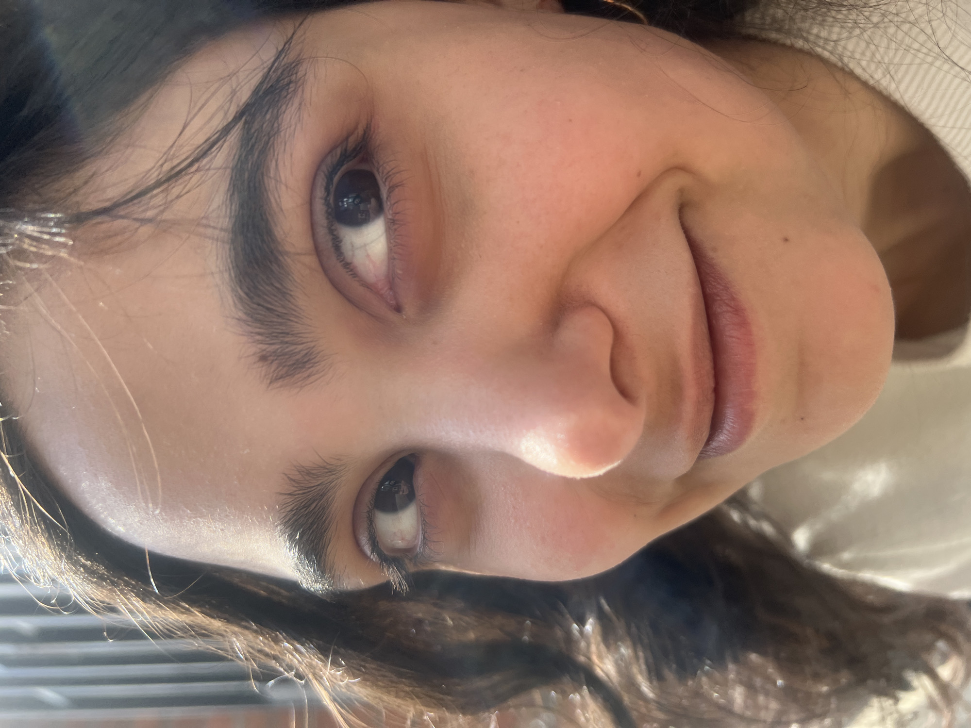 A close-up, angled portrait of a young woman with dark hair and dark eyes. The background shows indistinct shapes, but nothing that identifies a specific location in Tbilisi, Georgia. She is looking upward with a slight smile.