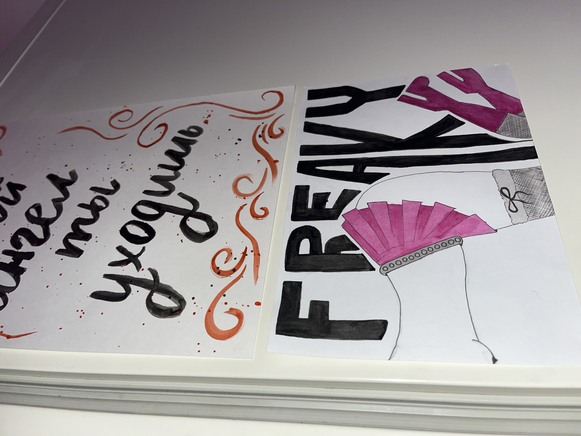 The image shows two pieces of paper on a white surface, likely a table or shelf. The paper on the left contains text in Cyrillic script, possibly Russian, with red and black ink splatters. The text translates to "How tired I am that you are leaving...". The paper on the right has the word "FREAKY" written in large, bold black letters, vertically oriented. An illustration of a woman's legs, wearing pink high heels, a pink fan-like accessory around one leg, and a garter with a bow is also present. The style is suggestive and artistic. The location is unknown, and there is no clear link to the city of Saint Petersburg, Russia.