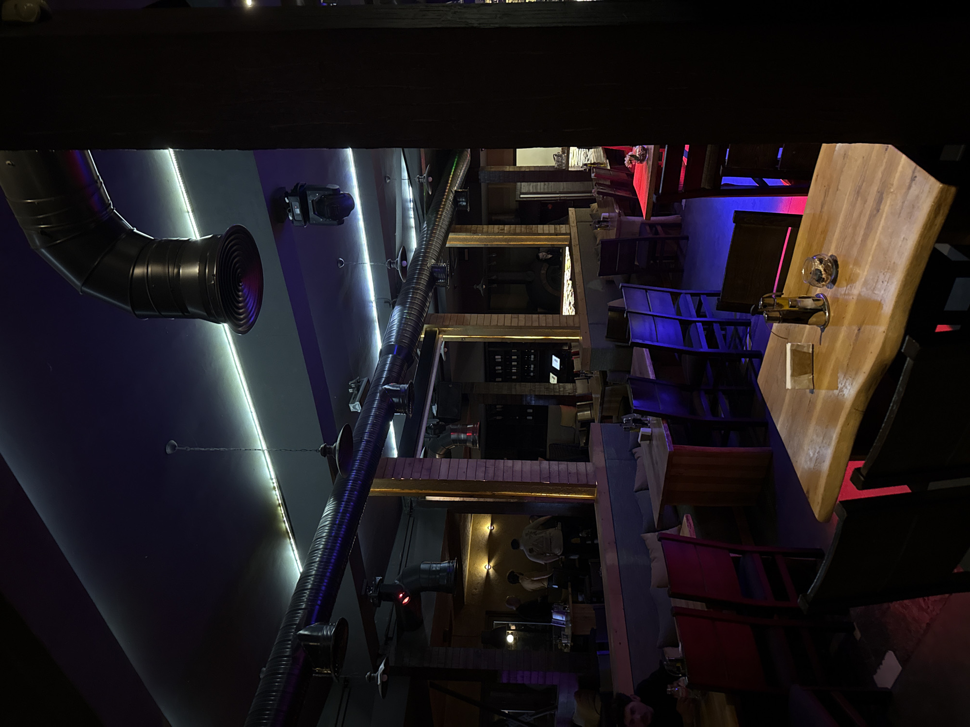The image shows the interior of a multi-level restaurant or bar in Sofia, Bulgaria. Visible elements include exposed industrial-style ventilation ducts running along the ceiling, metal light fixtures, and various tables and chairs. Lighting is a mix of white, blue, and red. There are people visible in different levels, but they are blurred. The overall impression is that of a modern, industrial-themed establishment.