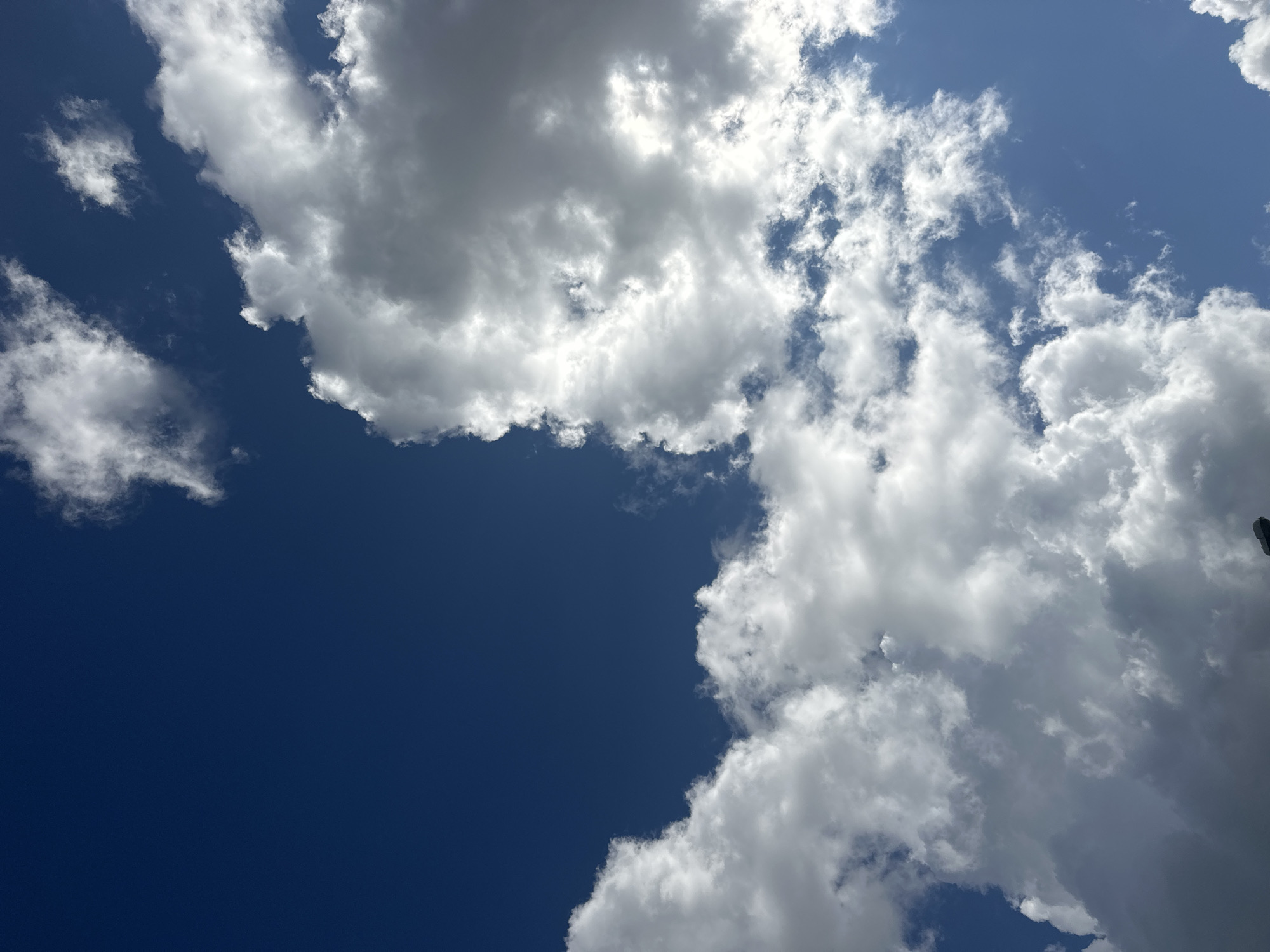 The image shows a view of the sky from ground level, looking upwards. The sky is a deep blue, with large, fluffy white clouds scattered across it. Some of the clouds are brightly lit by the sun, while others are in shadow, creating a contrast of light and dark. The clouds appear to be cumulus clouds, often associated with fair weather. There is no visible indication of the city of Minsk, Belarus, nor are there any people, subjects, or specific objects that could definitively place the image in that location. The scene is entirely focused on the sky and clouds.