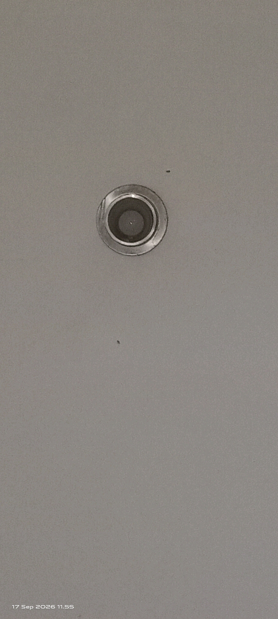 A ceiling-mounted, circular, metallic-trimmed light fixture is centered in the upper portion of the image, against a plain, light gray wall. Two small, dark specks, possibly insects, are visible on the wall surface, one to the upper left of the light and another below it. The lower right corner of the image displays a timestamp reading "17 Sep 2026 11.55". There is no visible indication of the city of Klaten, Indonesia within the image itself.