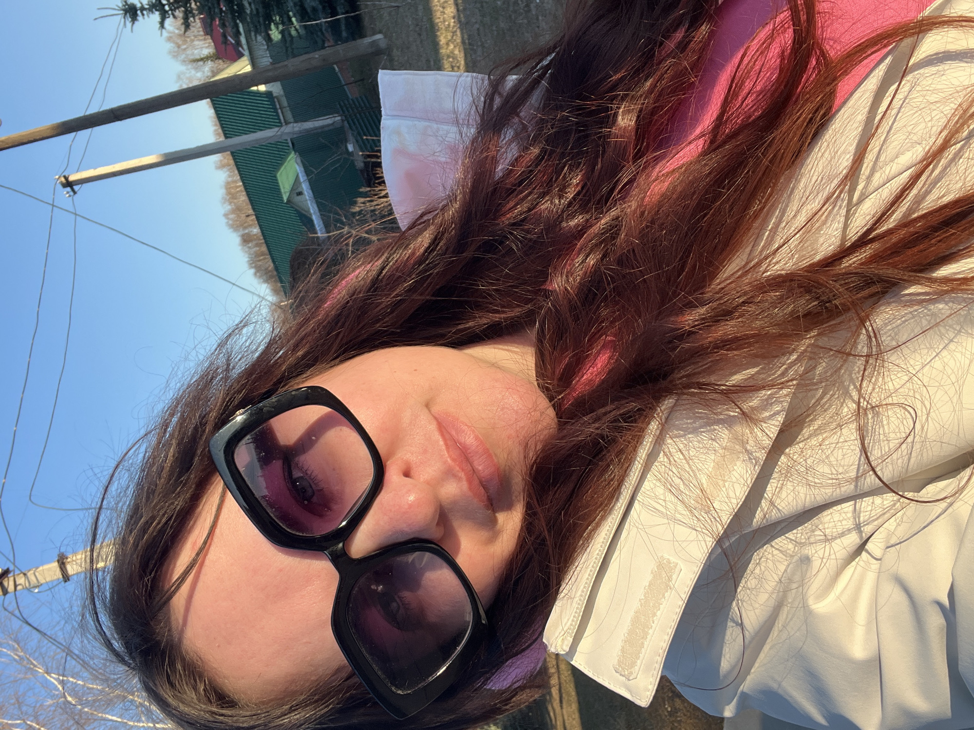 A person wearing sunglasses is lying on the ground. The background includes a blue sky, power lines, and a building with a green roof. The location is Noviy, Russia.