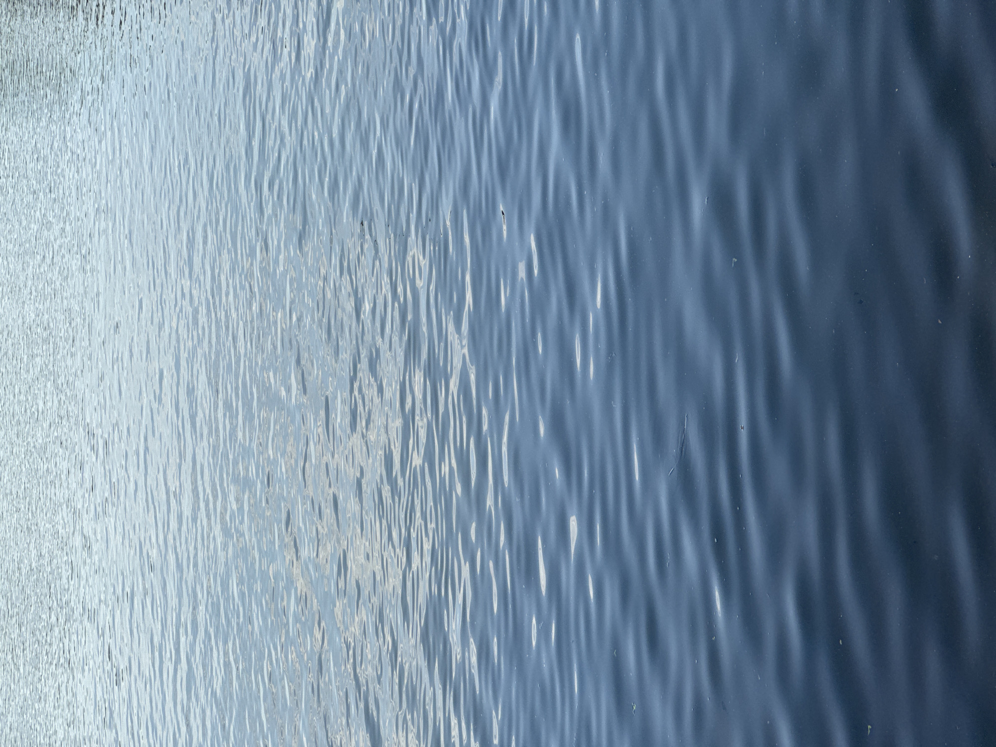 The image shows a close-up of rippling water. The color of the water is a light blue. The ripples create a pattern of light and dark areas across the frame. The location is not specified.