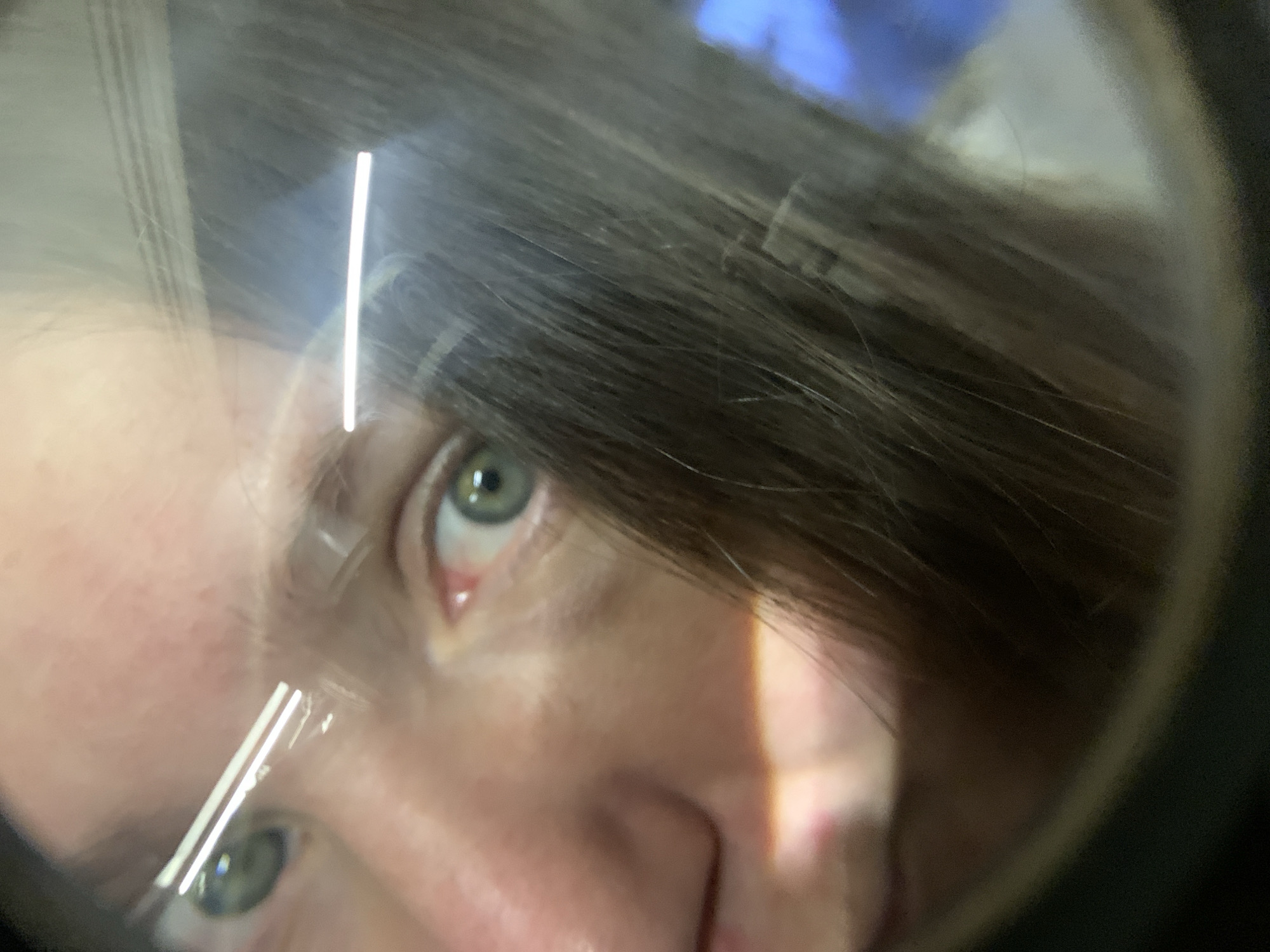 A close-up photograph of a person's face, appearing as if viewed through a magnifying glass or similar lens. The person has light skin, green eyes, and brown hair. The image is slightly distorted due to the lens, and bright light reflects off the lens's surface. The nose and right side of the face are prominent, while the left side is somewhat obscured by the lens and hair. There is no information available to determine the location of the image in the city of Zasechnyi, Russia.