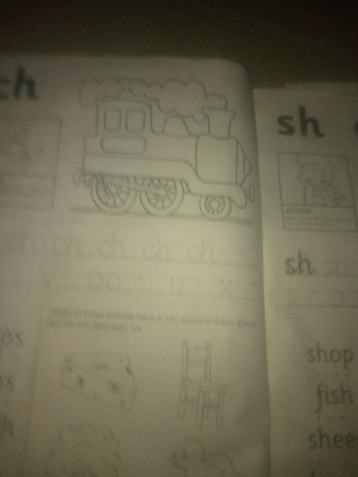 The image shows a page from a children's educational workbook. On the left side, a drawing of a steam train is prominent. Below the train, there are handwritten letters "ch" repeated several times, followed by other letters and symbols that are difficult to decipher. Further down on the left, there are drawings of a slice of cheese and what appears to be a cloud or wool.
On the right side of the page, the letters "sh" are written, followed by the words "shop," "fish," and "sheep." There is also a small drawing of a person in a box with the word "ACTION" below it, and some illegible text.
The image is slightly blurry and appears to be taken in low light conditions. The paper is white and shows signs of normal use. There are no specific identifiable landmarks or contextual elements that would allow for the determination of its location in Jauro Yinu, Nigeria. The content of the page is educational, focusing on early literacy and phonics.
