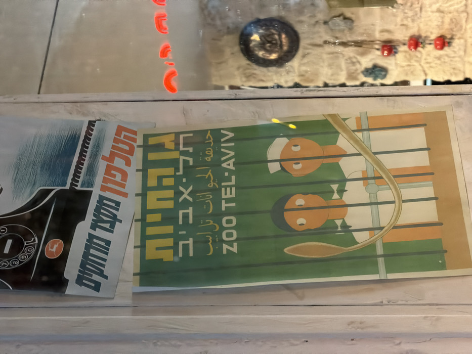 The image shows two vintage posters. One is of an old-fashioned black telephone with Hebrew text: "הטלפון מקצר מוחקים" (The telephone shortens distances). The second poster, in green and yellow, is for the "ZOO TEL-AVIV" with corresponding text in Hebrew and Arabic: "גן החיות תל-אביב" and "حديقة الحيوانات تل ابيب". The poster includes a simplistic illustration of two figures behind bars.