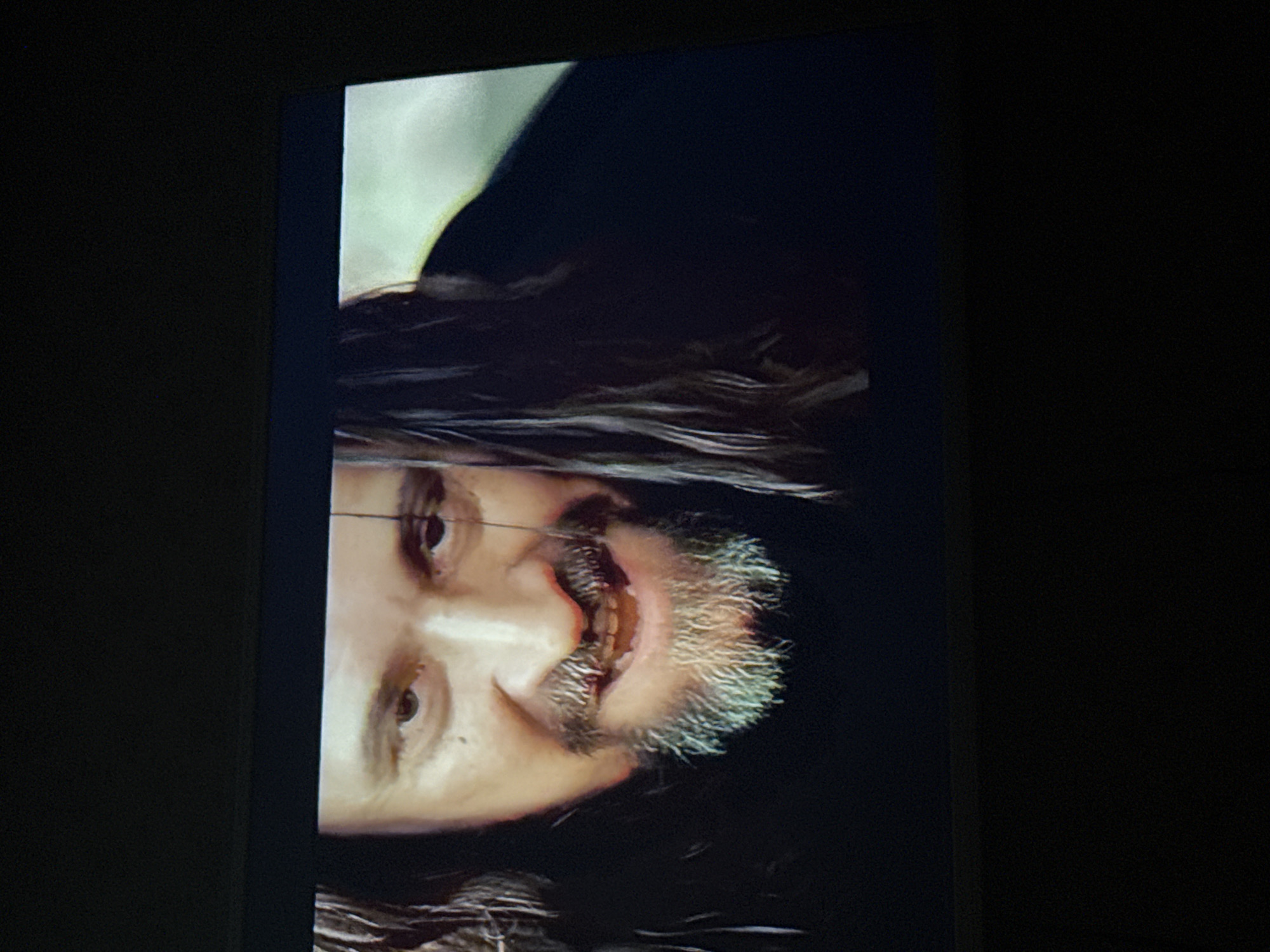 A man with long hair and a graying beard is displayed on a screen. The screen is surrounded by dark space. The image provides a close-up view of the man's face. There is no information to determine this image was taken in the city of Mytishchi, Russia.