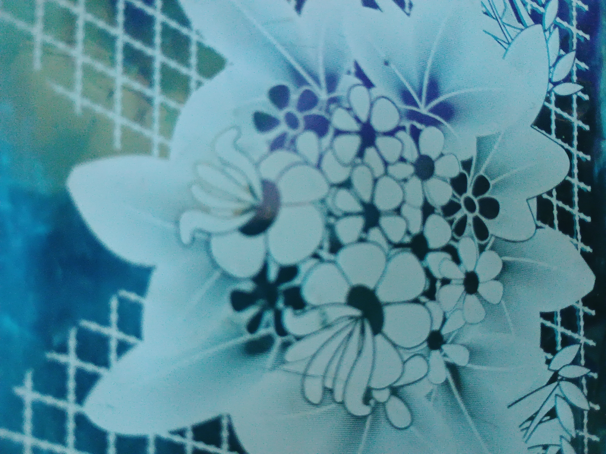 The image is a close-up, oblique view of a light blue and white floral pattern on what appears to be fabric or a tablecloth. The pattern features stylized flowers with dark centers, varying in size and arrangement. Some larger, more detailed flowers are visible, as are clusters of smaller, simpler blooms. In the background and edges, a subtle grid-like pattern is present, potentially representing a netting or lace overlay. The lighting is somewhat diffuse, giving the image a soft, slightly hazy quality, with a predominant cool blue and white color palette. There is no indication of any specific location within the city of Zaporizhzhia, Ukraine, or any contextual elements that would suggest a particular environment or activity.