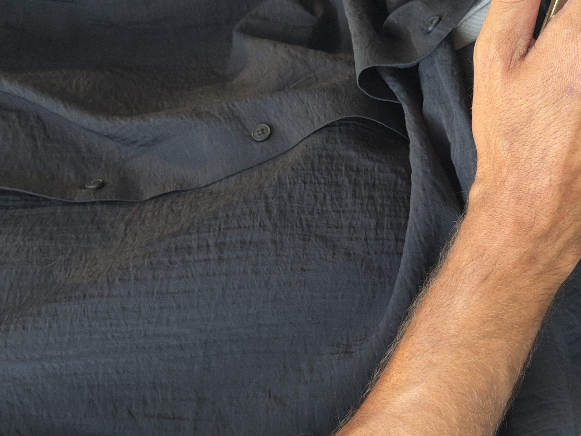 The image shows a close-up of a person's arm and torso, wearing a dark-colored, textured shirt with buttons. The arm is hairy and tanned, and the shirt appears to be made of a crinkled fabric. There are no discernible features indicating a specific location within Barcelona, Spain.