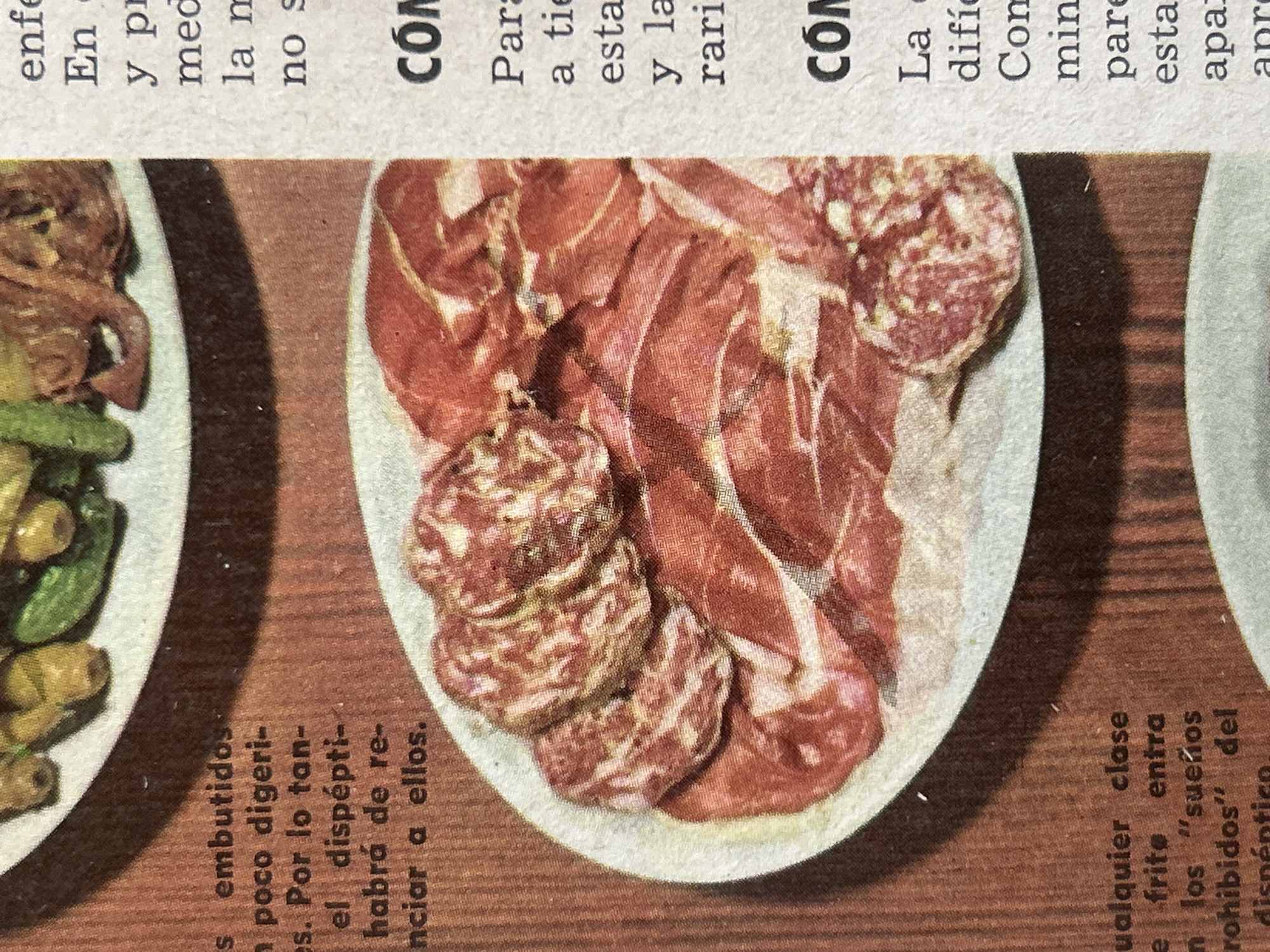 The image is a close-up photograph of a plate of sliced cured meats and a portion of a newspaper. The plate contains several circular slices of salami with a visible white fat marbling and larger, thinner slices of a reddish cured meat that appears to be ham or prosciutto. The meats are arranged on a white oval plate. In the background, a portion of a newspaper is visible with text in Spanish. The newspaper column on the right has headings like "CÓM" and "LA" followed by several lines of text. The newspaper on the left is mostly obscured by the plate but shows text that includes "s embutidos," "poco digeri-," "el dispépti-," and "nciar a ellos." There is no visible indication of the city of Santa Ana, Venezuela, in the image.